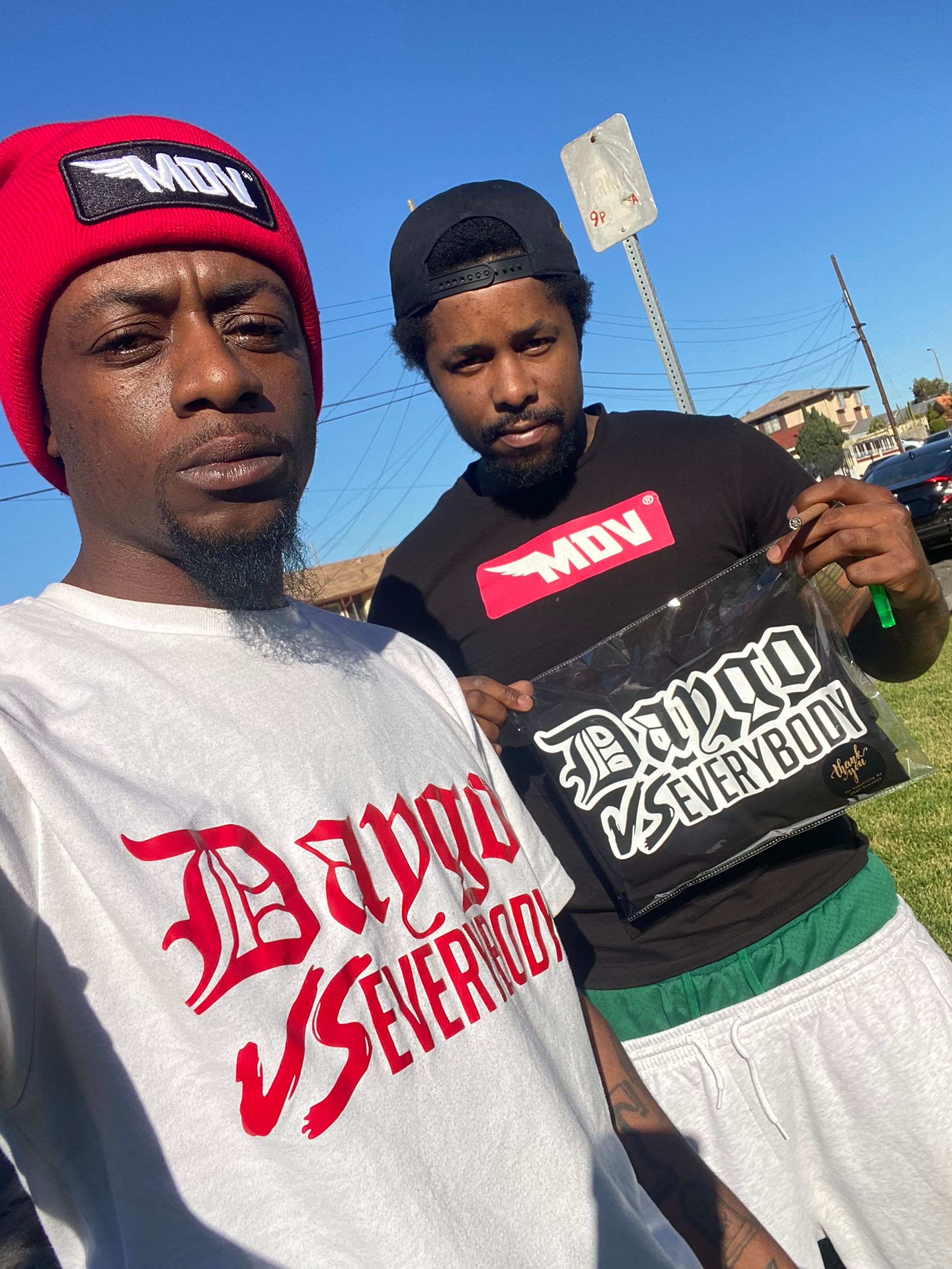 Two young men outdoors holding a sign with text, against a blue sky background.
