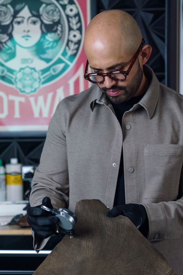 Man with glasses and bald head wearing gray shirt, handling fabric in workshop.