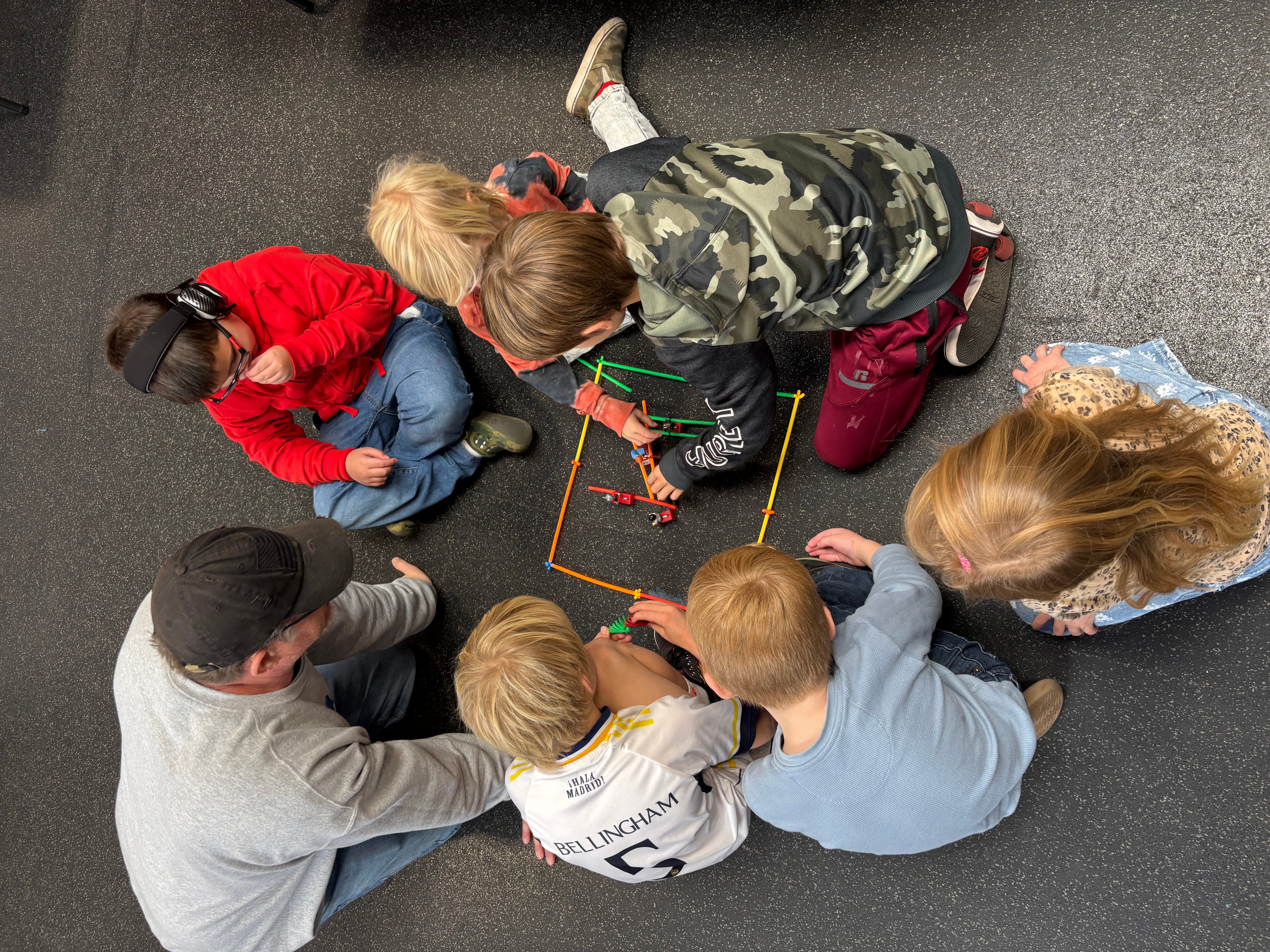 Group of children and adults sitting on the floor, drawing with colorful markers on paper, engaging in a collaborative activity.