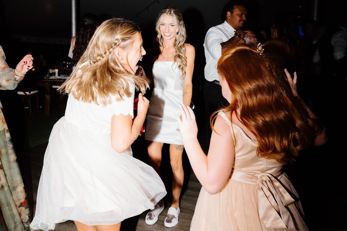 Three women dancing and smiling at a party, with other people in the background.