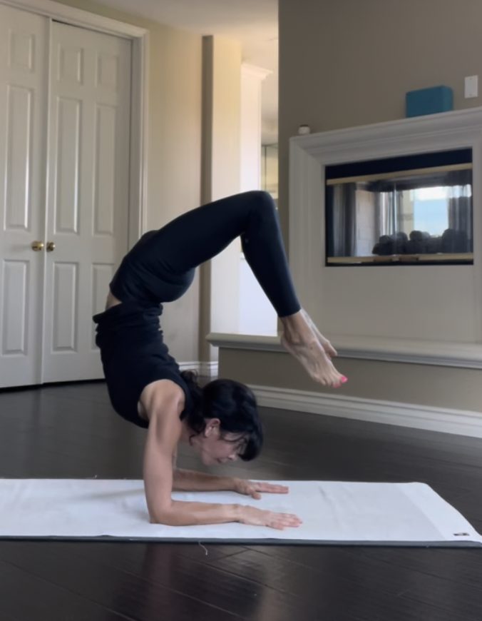 Woman performing a yoga pose on a white mat indoors, with a fireplace and closed door in background.