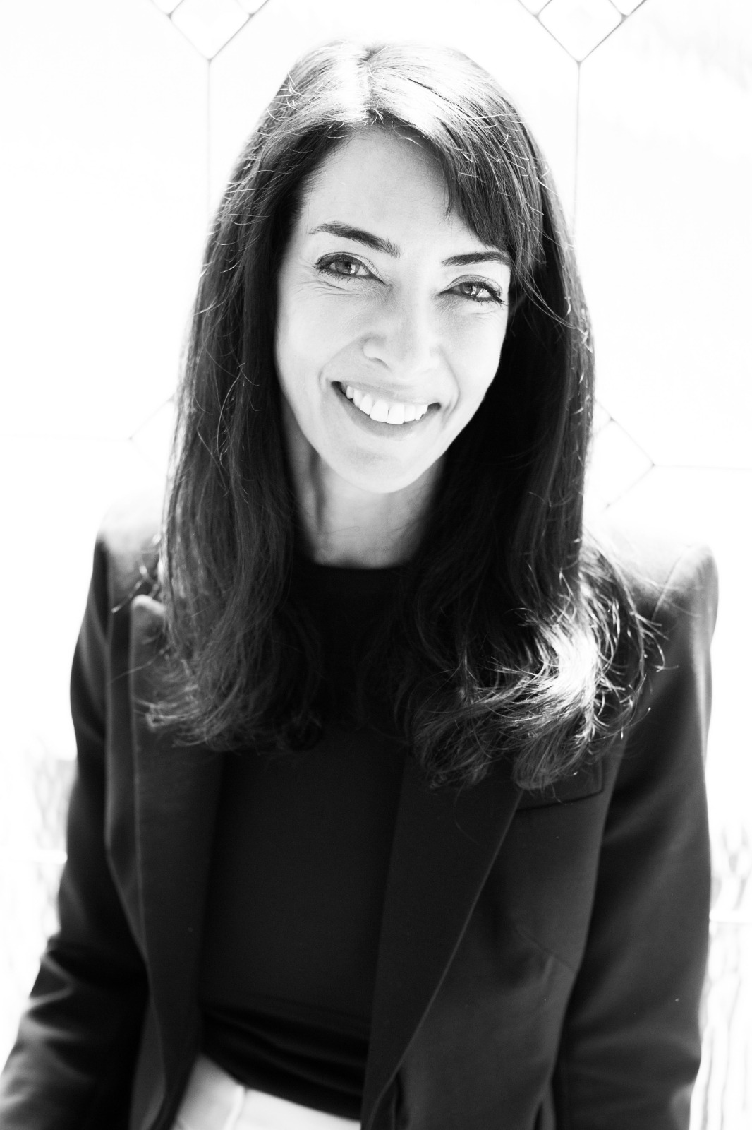Woman with long hair smiling, wearing a blazer, in black and white.