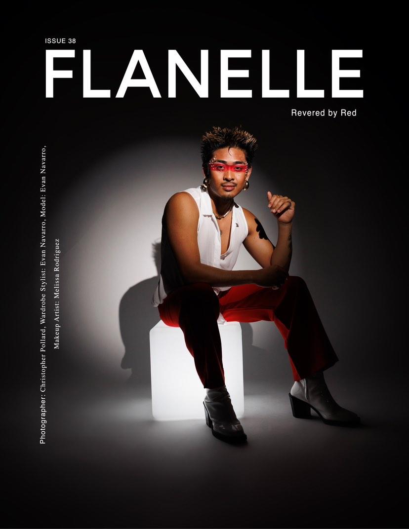 Woman sitting on a white block, wearing glasses, sleeveless top, and dark pants, against a dark background.