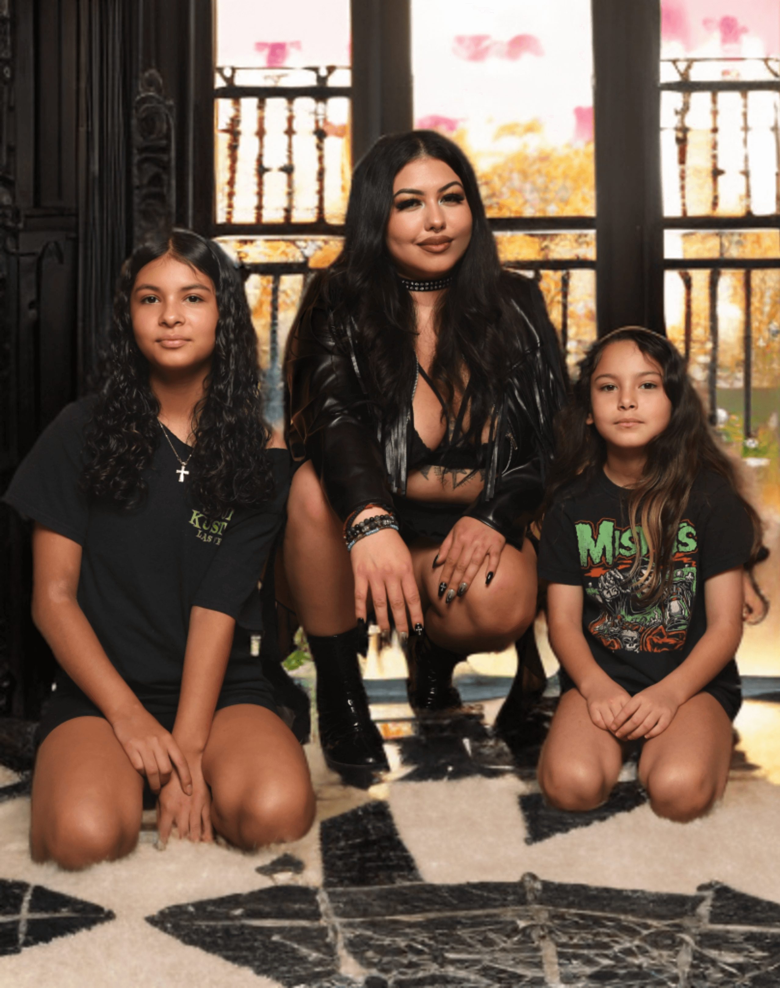 Three females sitting on a patterned rug in front of large windows with a balcony view, autumn trees outside.