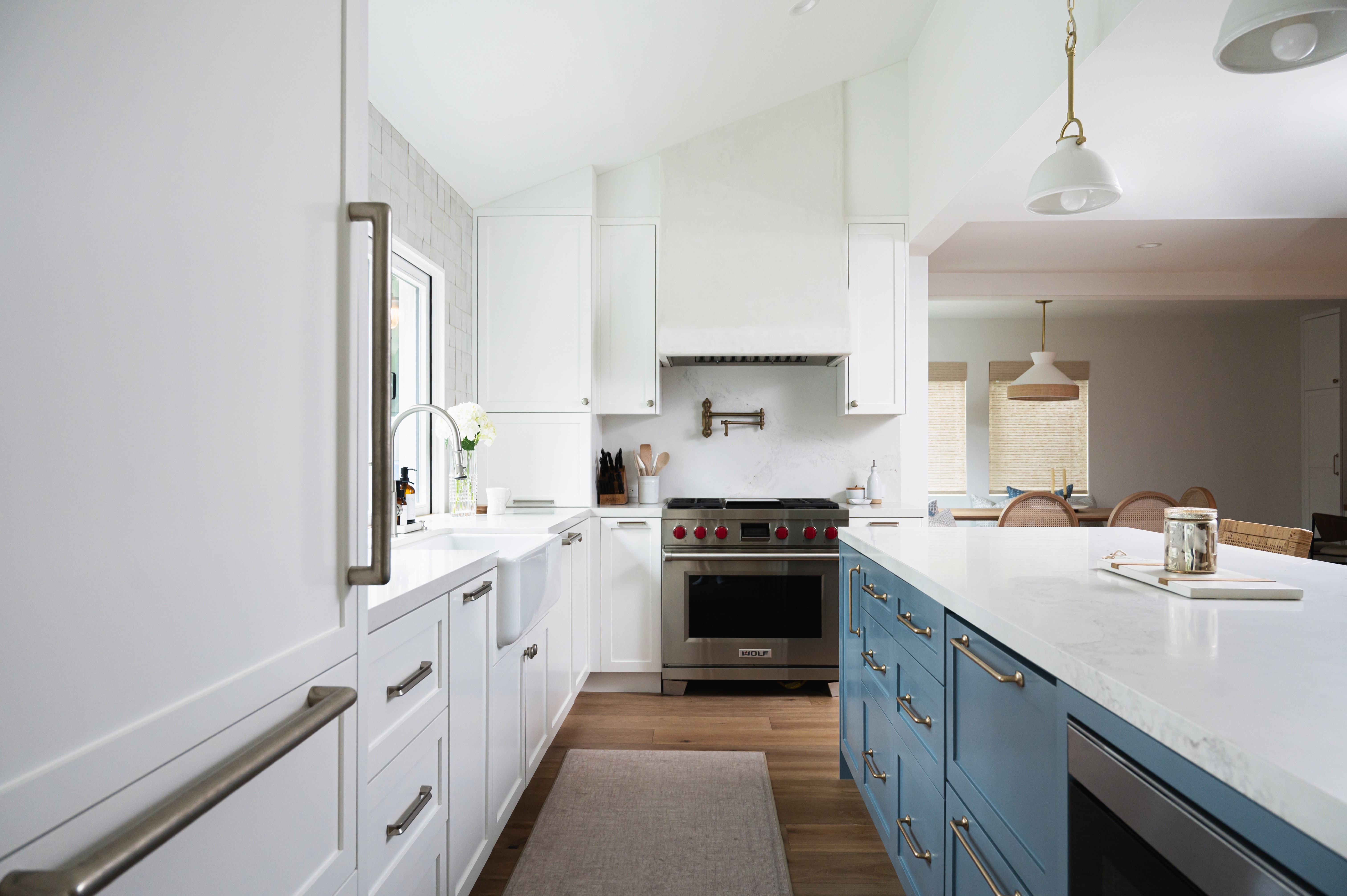 Bright kitchen with white cabinets, a blue island, and a window above the sink, with a stove and pendant lights.
