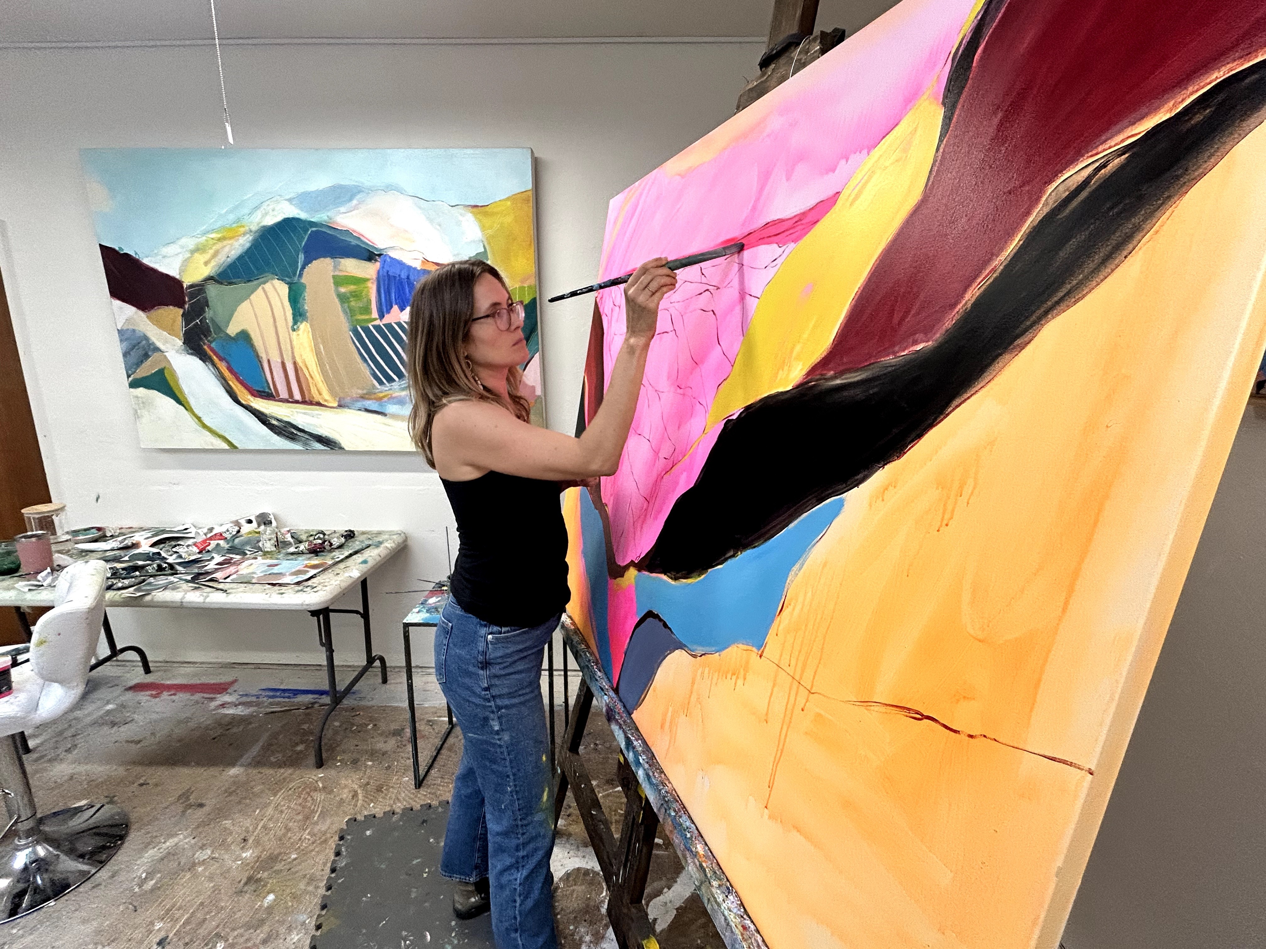 Woman painting a large colorful abstract artwork on a canvas in an art studio.