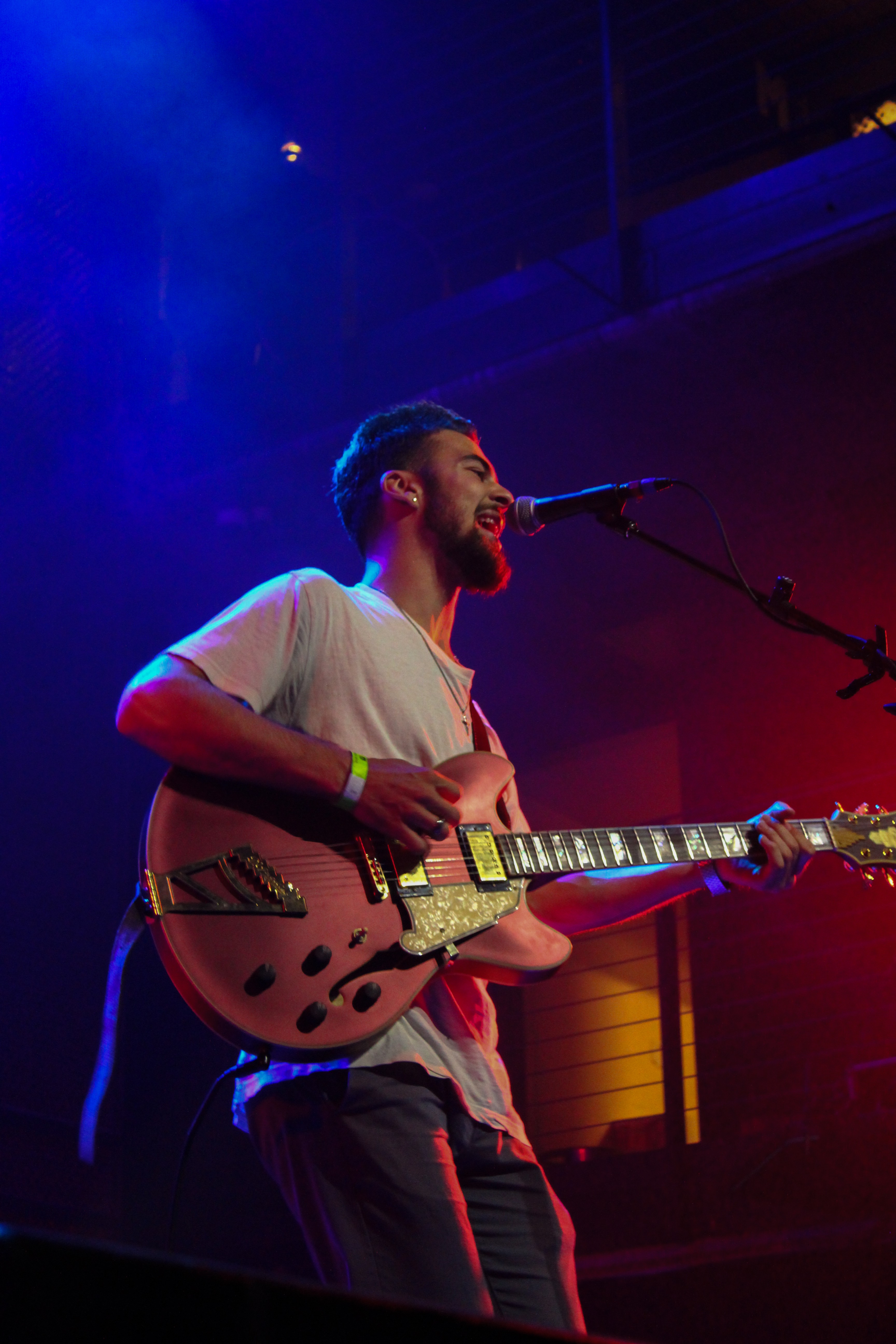 Male musician singing into a microphone while playing an electric guitar on stage with colorful lighting.