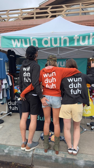 Group of people wearing black and red shirts with white text, standing under a teal and white tent.