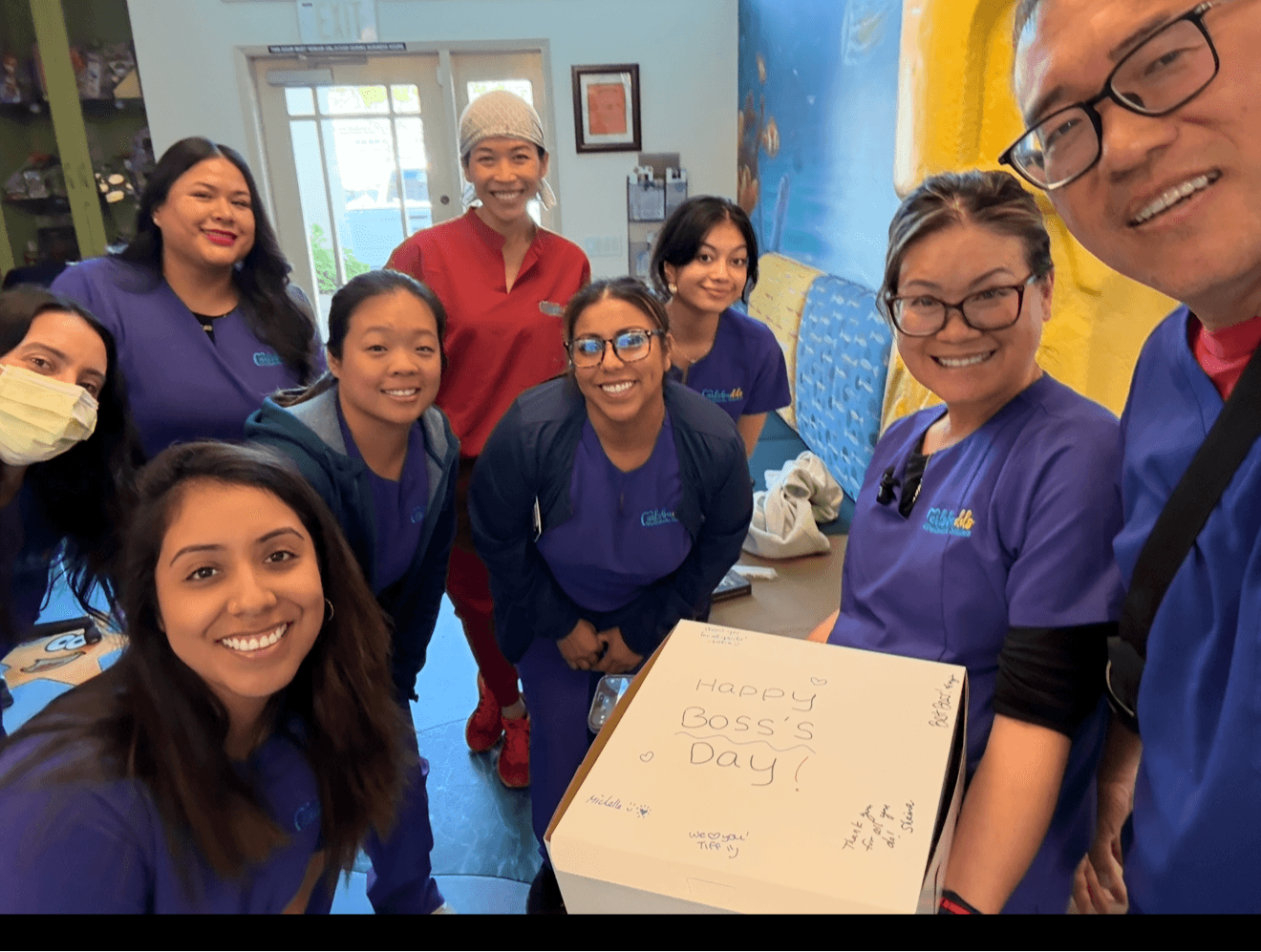 Group of nine diverse women and girls smiling around a box in a colorful room.