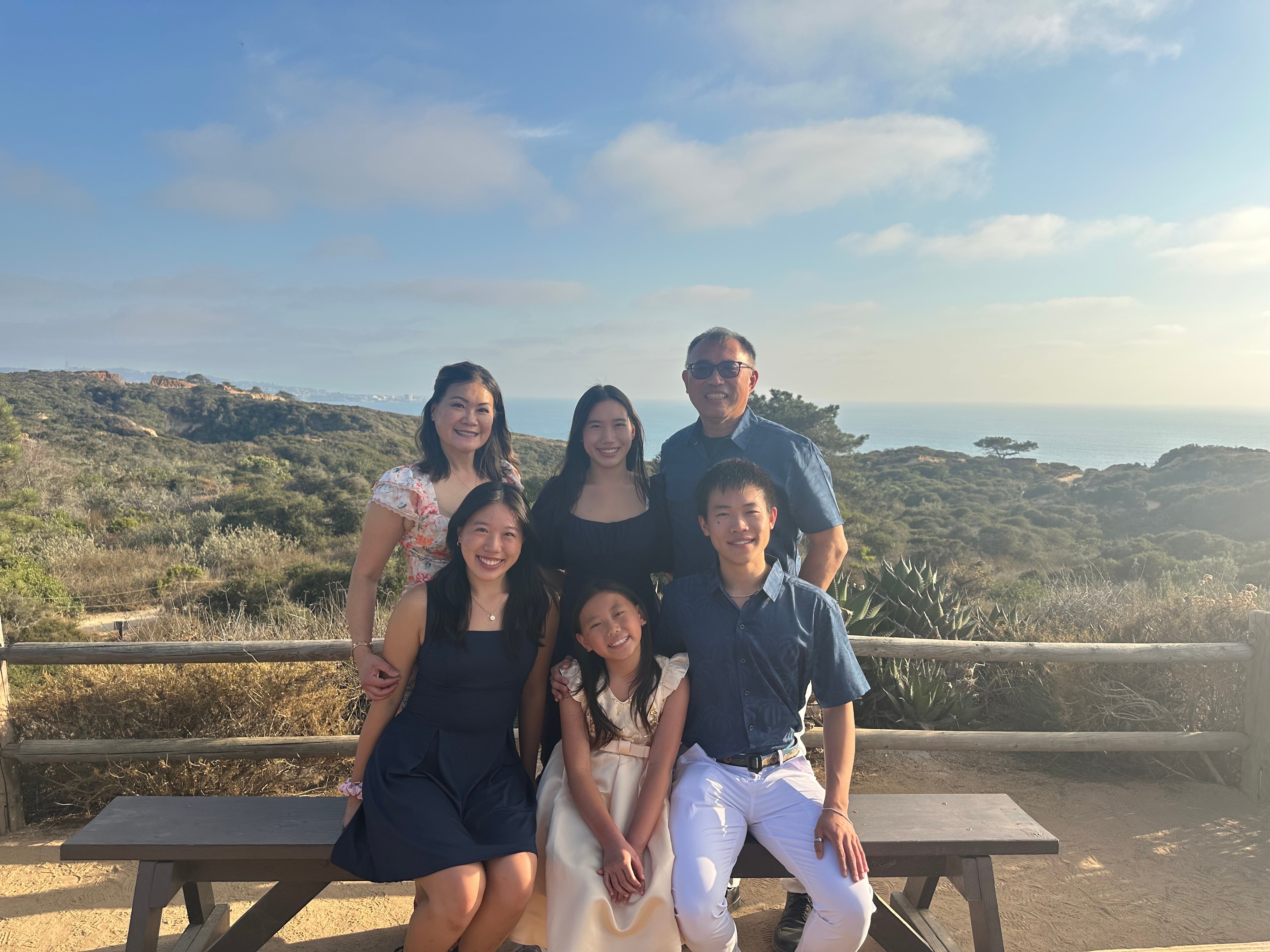 Group of five people sitting and standing outdoors with a landscape and ocean in the background.