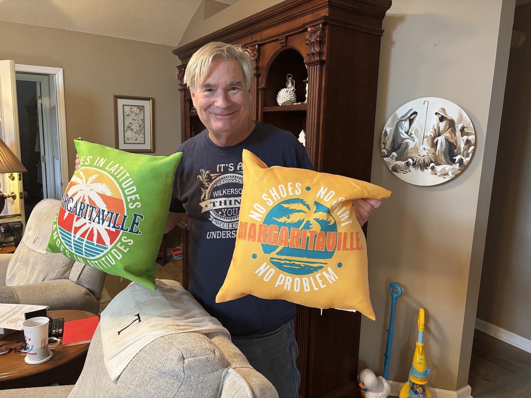 Man holding two colorful pillows with beach and ocean designs in a living room.