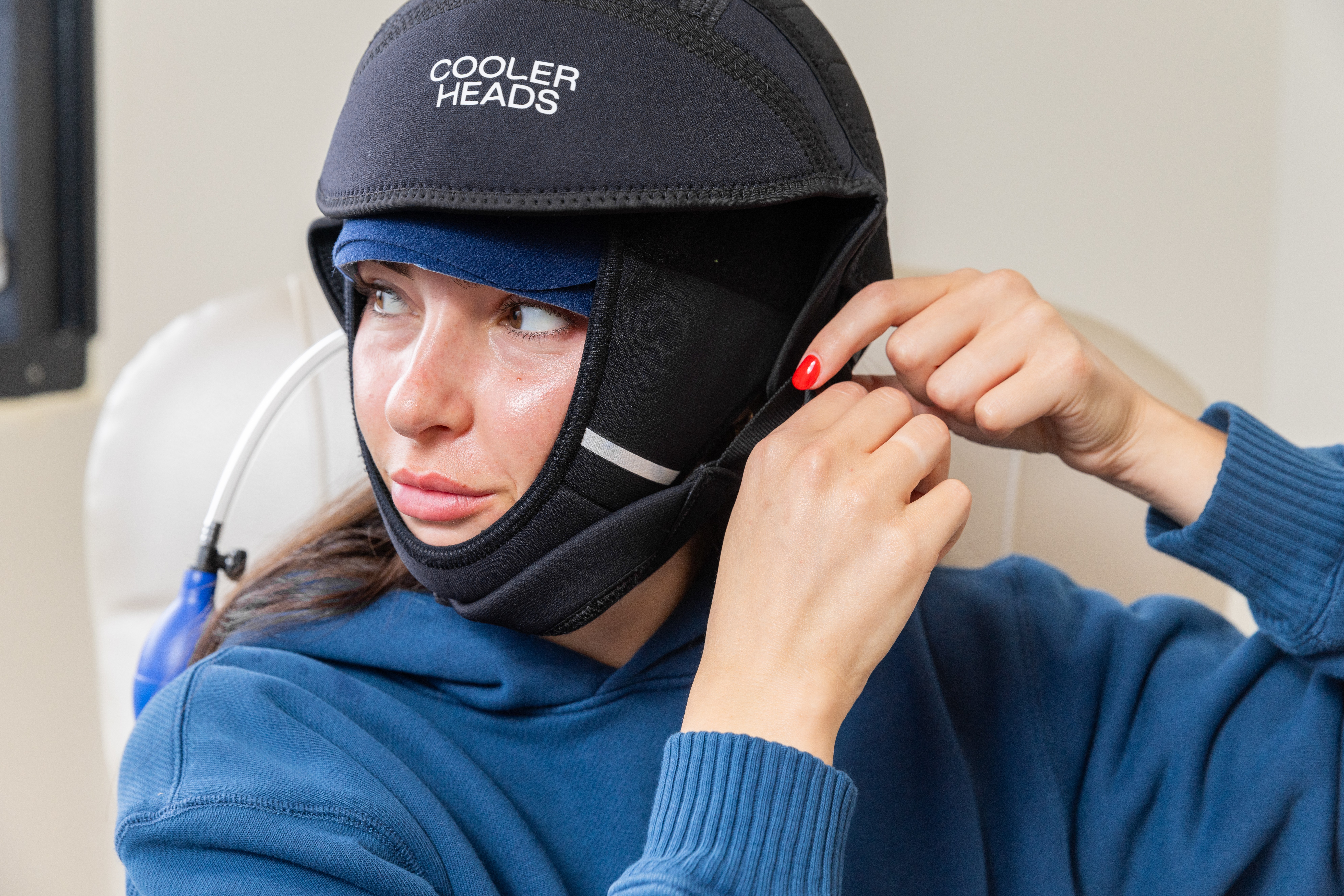 Person wearing a helmet labeled 'Cooler Heads' adjusting the strap, with a focused expression, in a clinical setting.