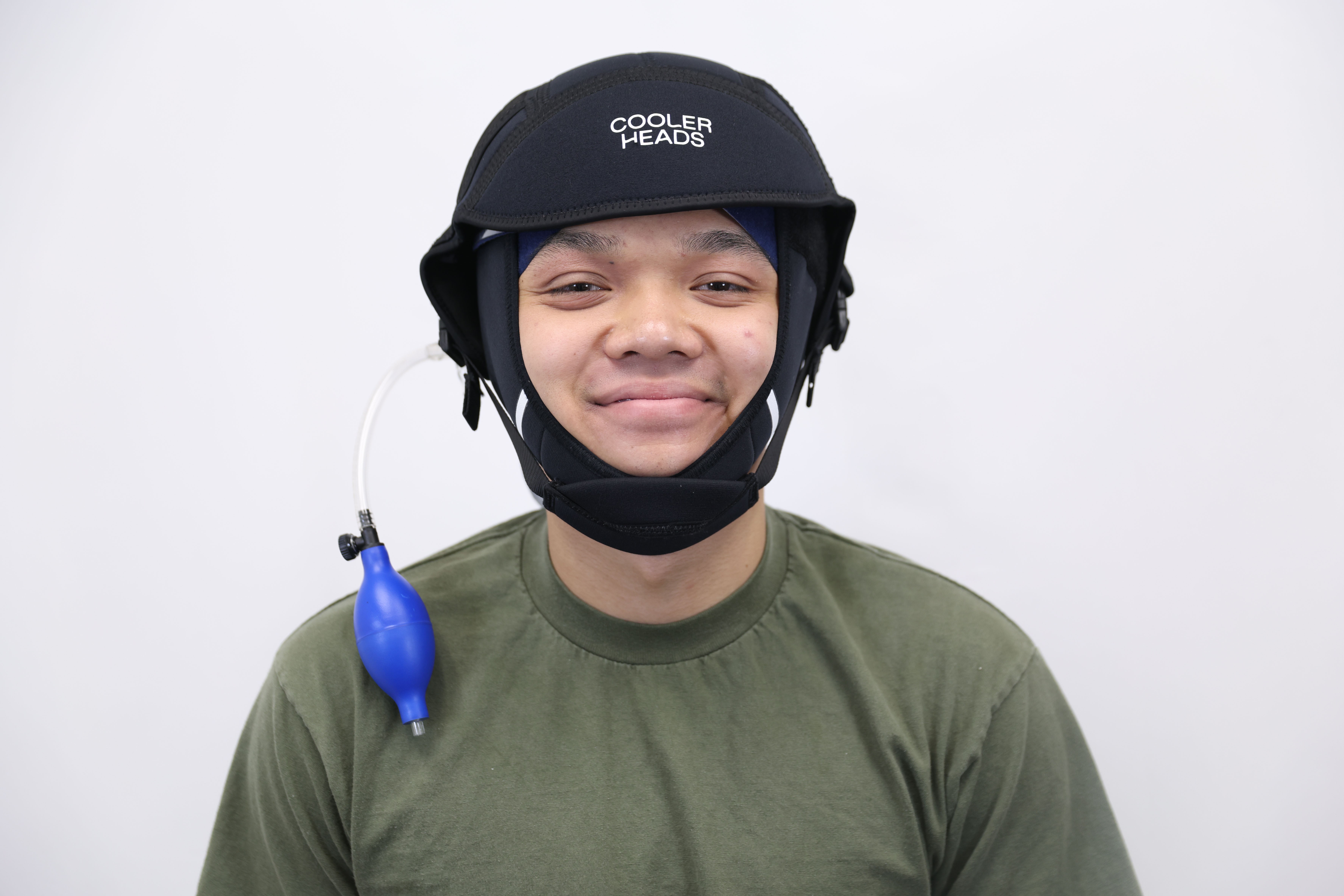 Person wearing a black helmet with a logo, green shirt, and a blue water balloon attached to their shoulder, smiling.