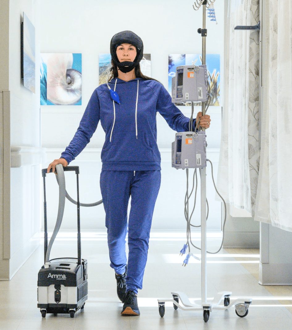 Woman in medical setting with headgear, standing next to medical equipment, holding a device, in a bright room with artwork on walls.