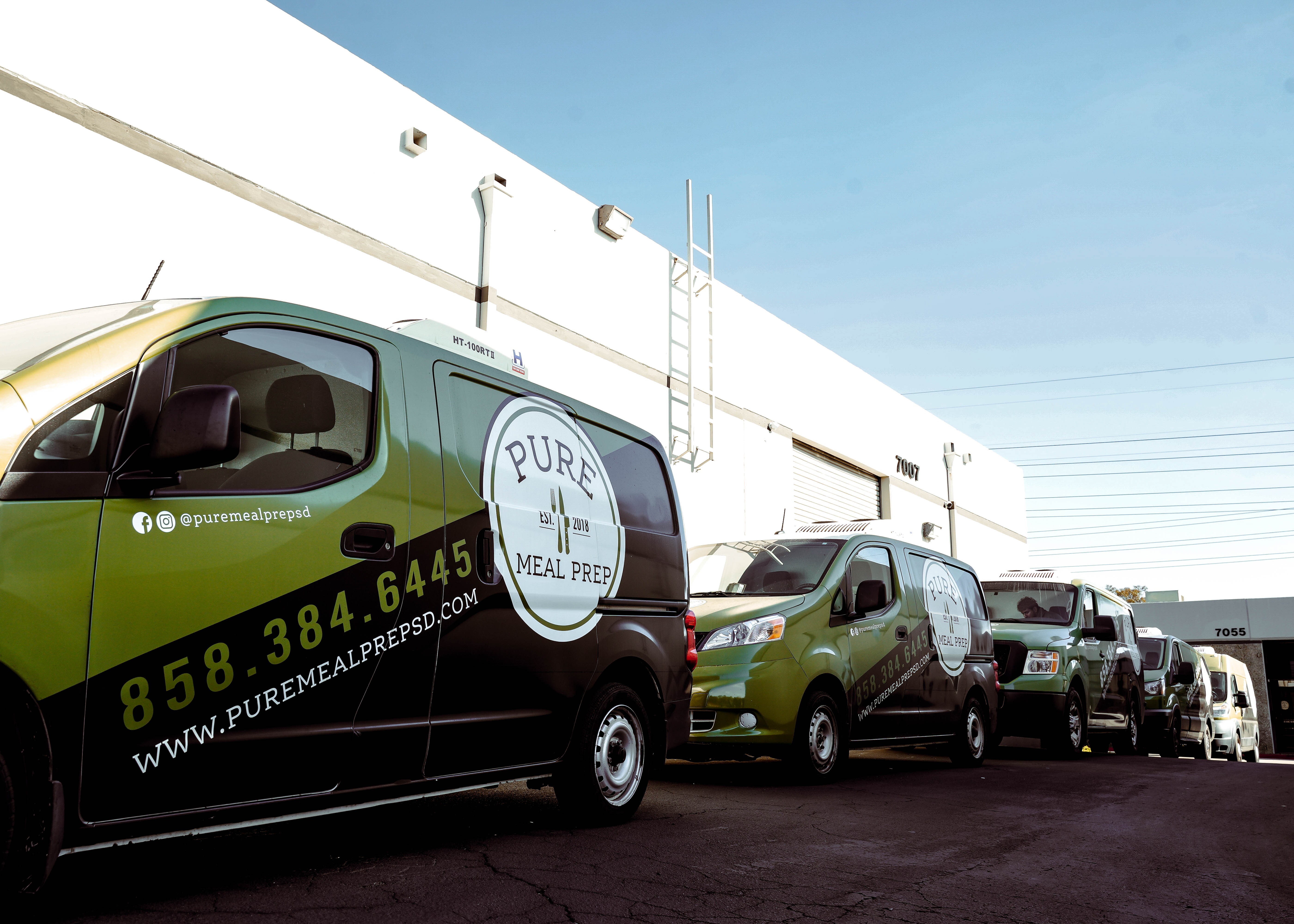 Line of vehicles parked outside a building, including a green van with a logo and contact information.
