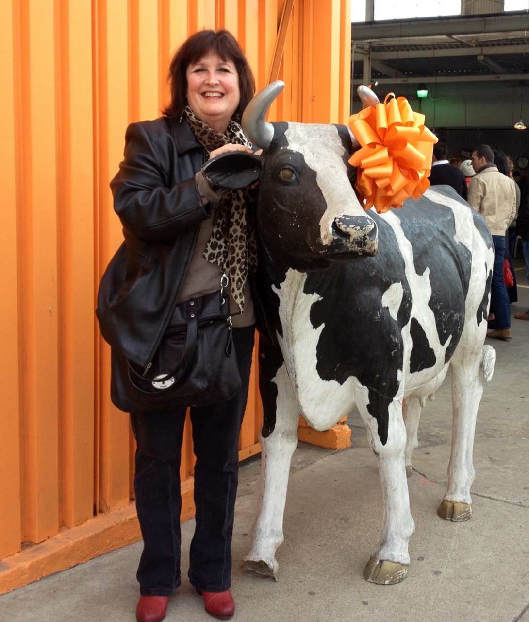 Woman standing next to a cow statue decorated with an orange bow, smiling, in front of orange wall panels.