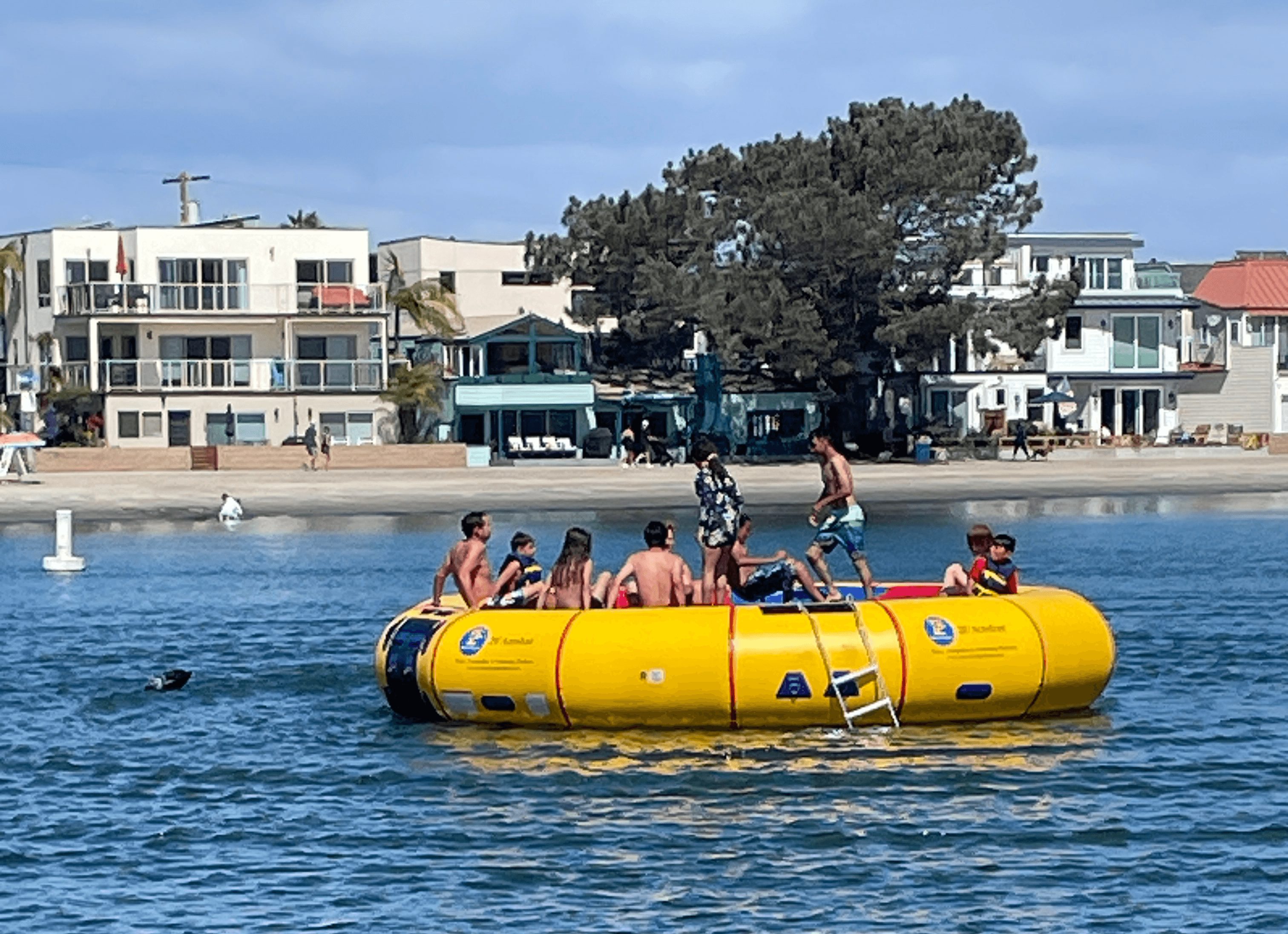People on a yellow inflatable boat in water with buildings and trees in background.