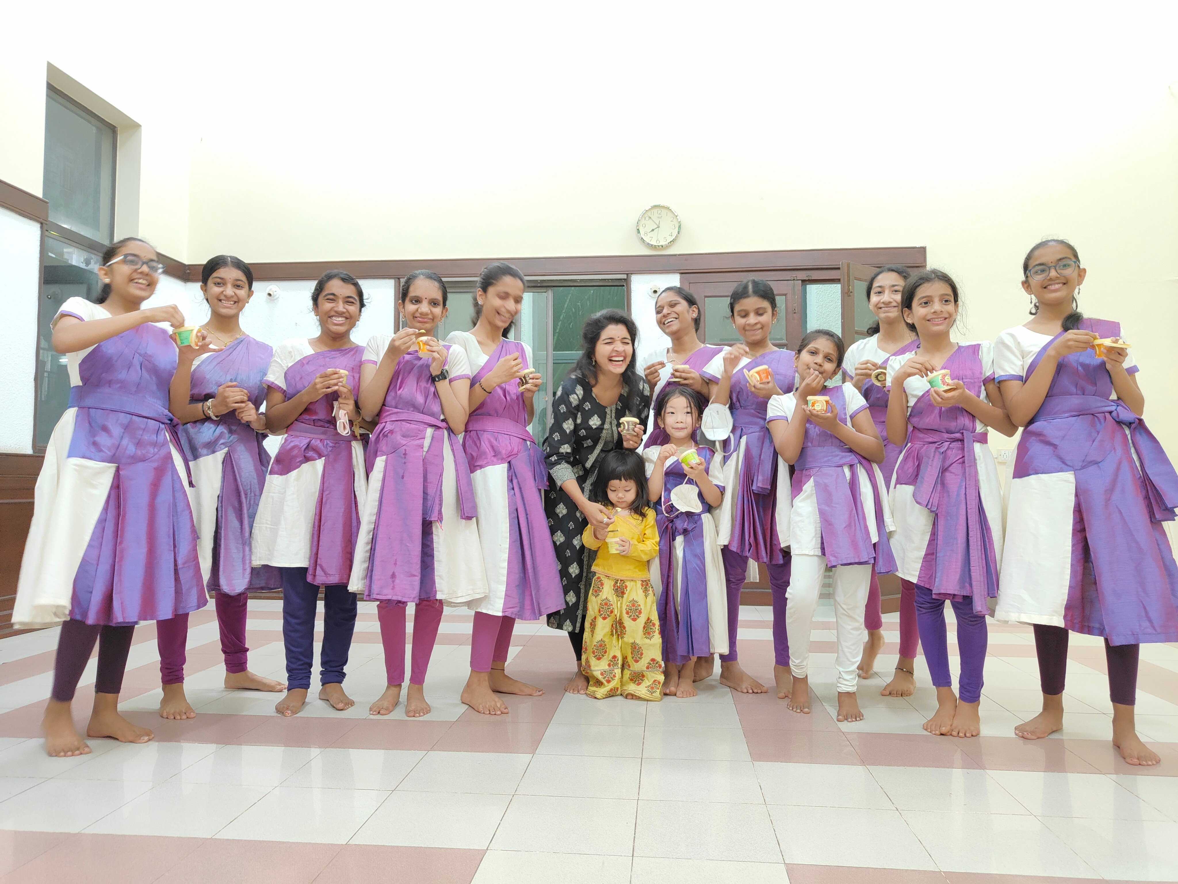 Group of women and children in purple and white uniforms holding gifts, standing indoors in a line.