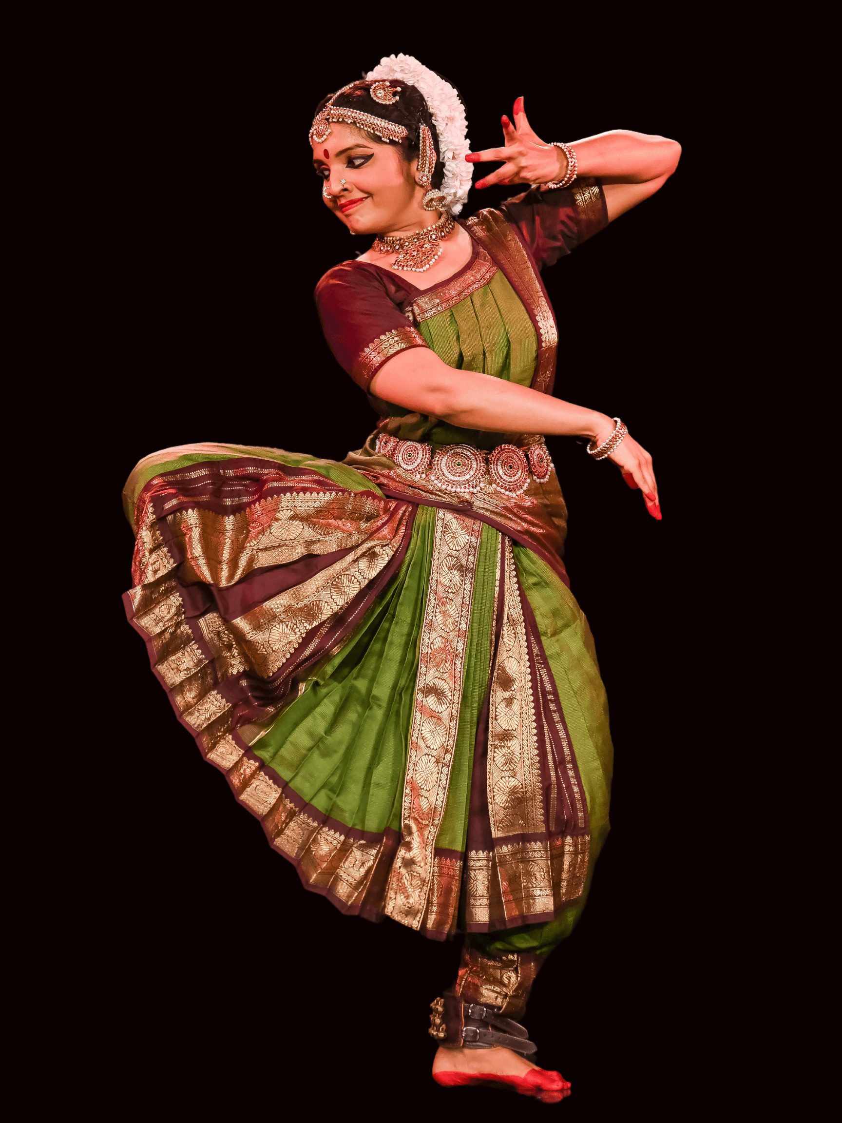 A woman in traditional Indian dance attire performs a dance pose with a dark background.