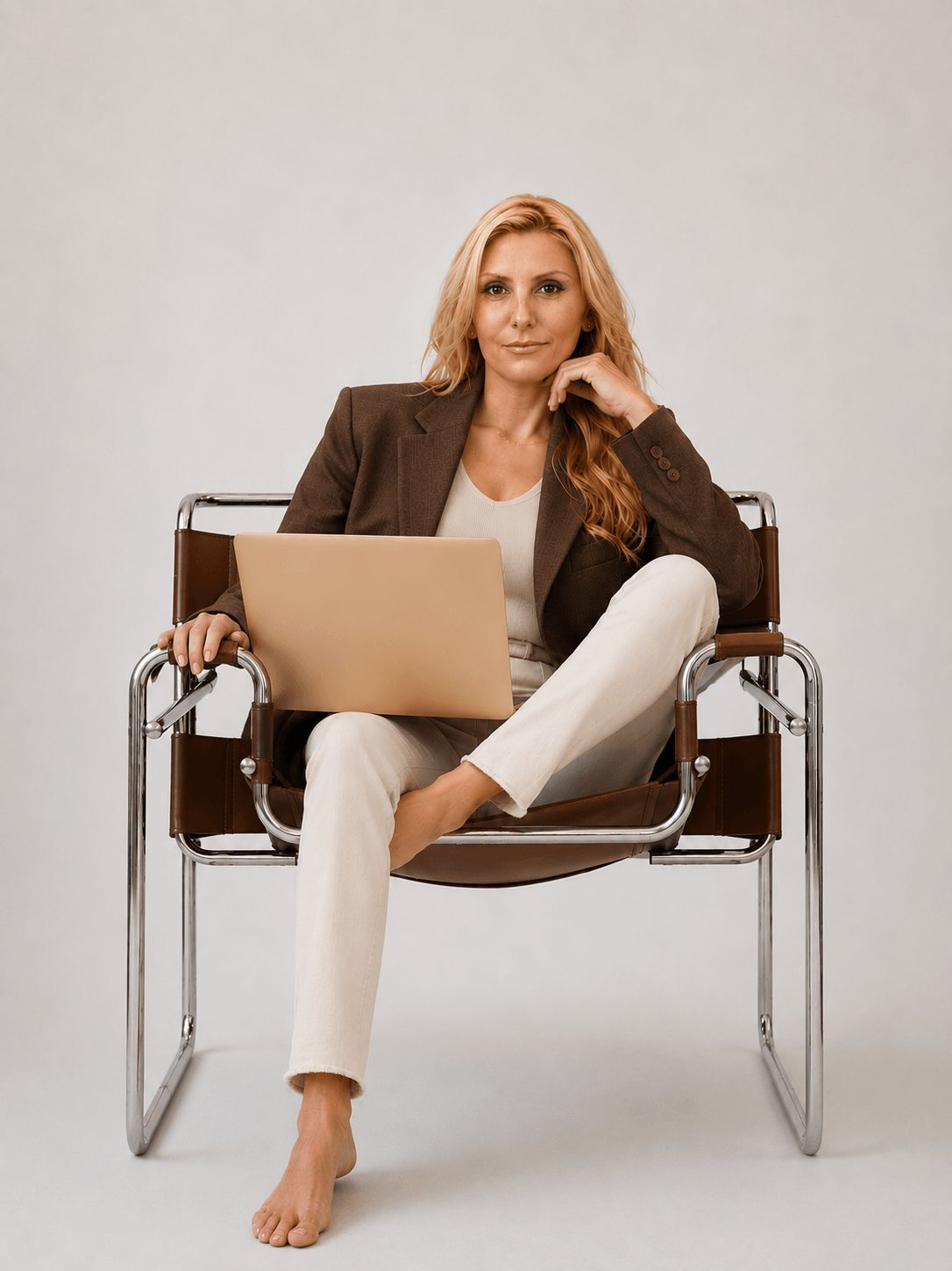 Woman sitting on a chair with a laptop, smiling, with a neutral background.