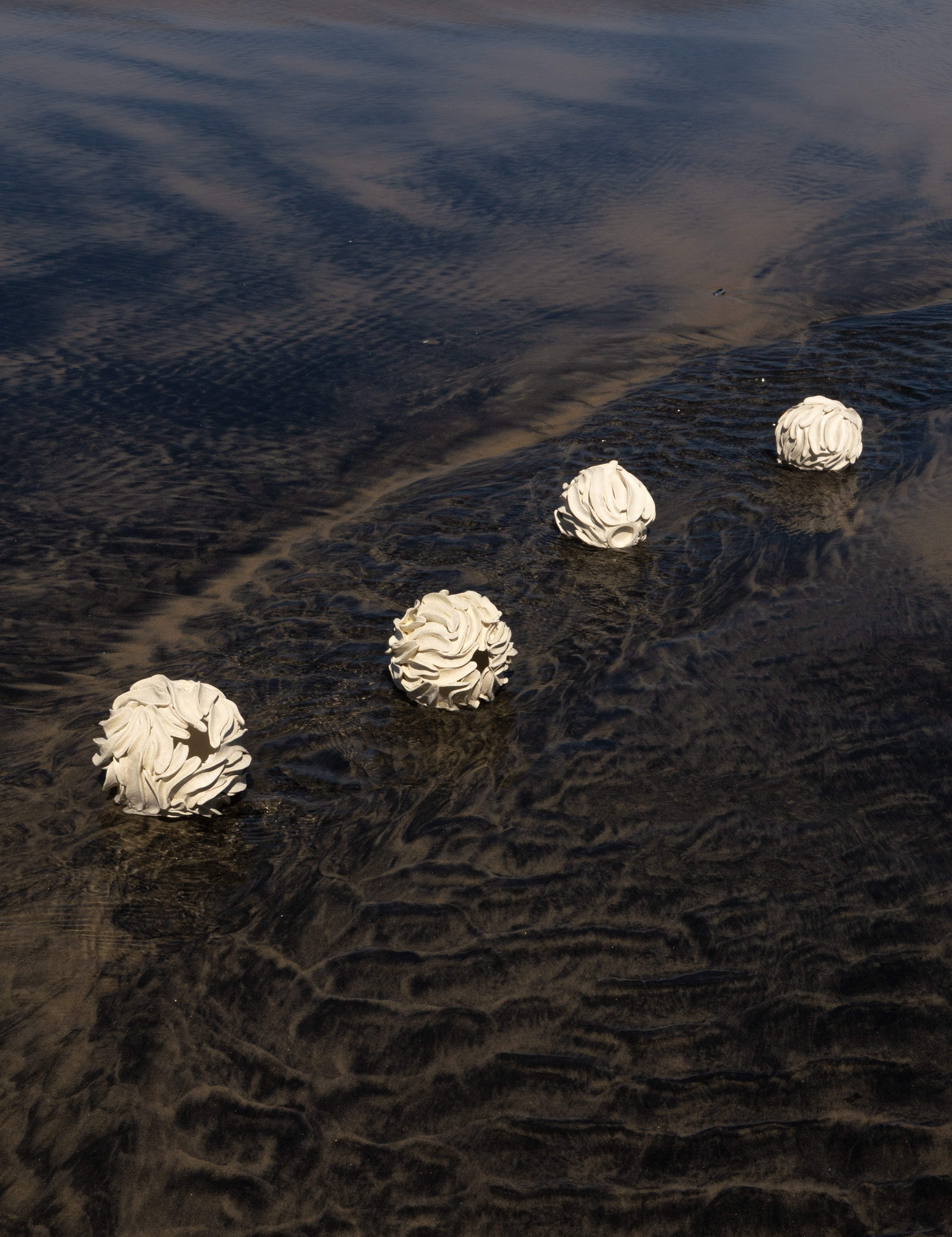 Four white spherical objects floating on water with ripples and reflections, arranged in a diagonal line.