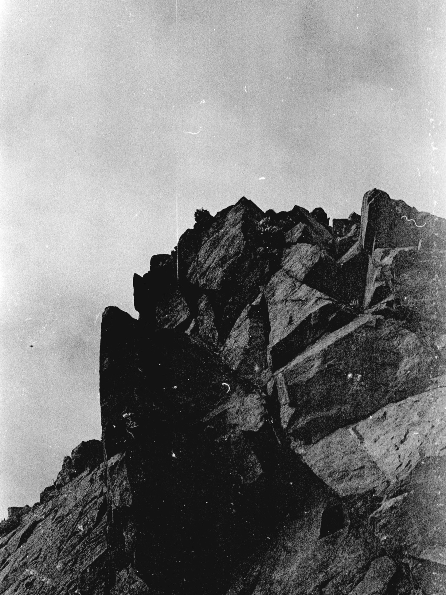 Cliffside with jagged rocks and a cloudy sky above, black and white photograph.