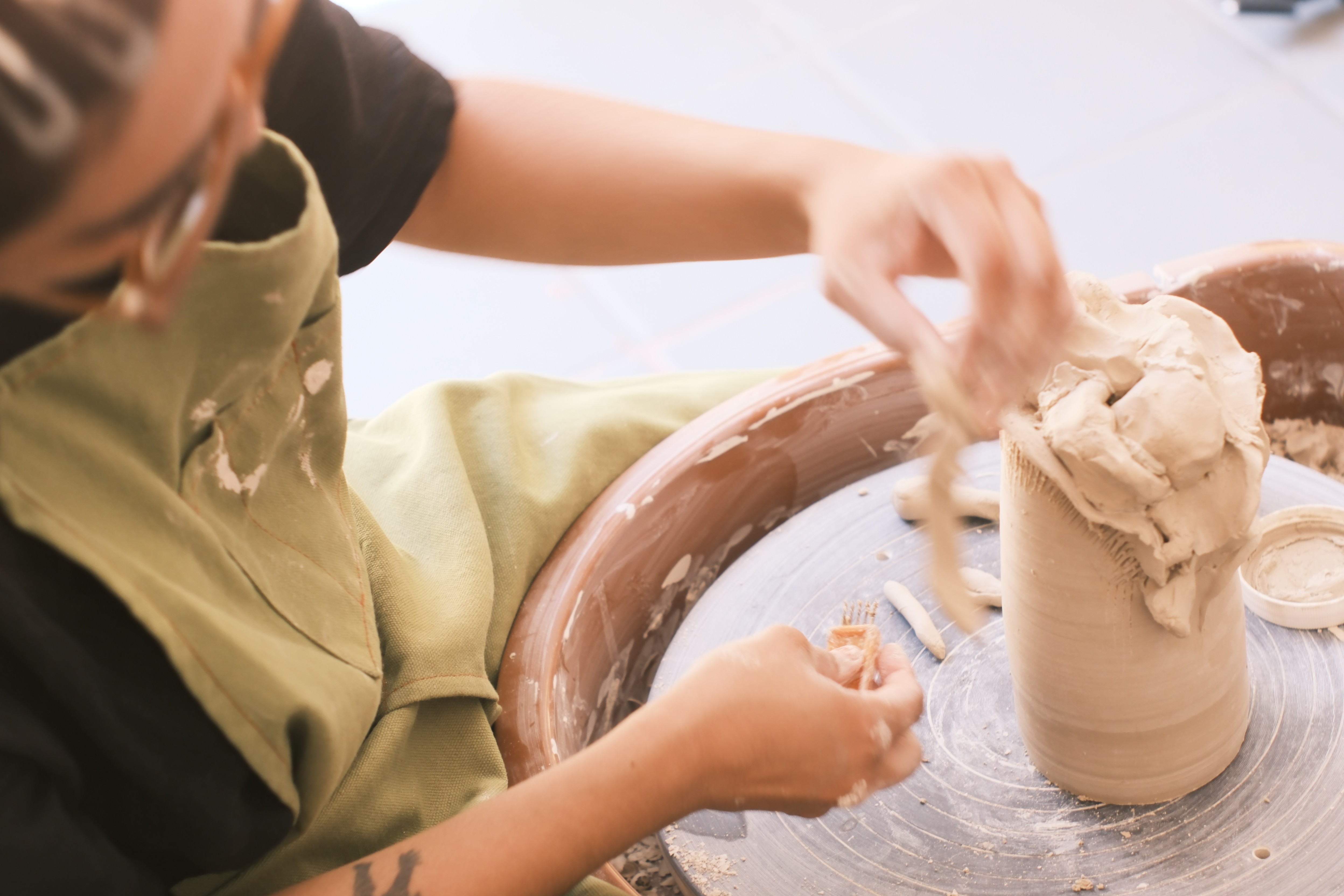 Person shaping clay on a pottery wheel with hands covered in clay, wearing an apron.