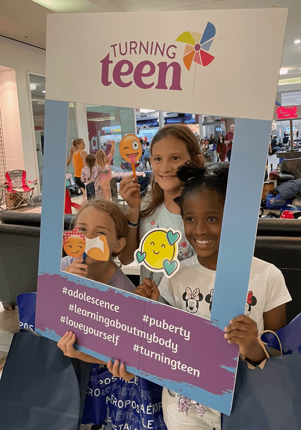 Three children holding a frame with a sign that reads 'Turning teen' and hashtags, smiling and posing for a photo.