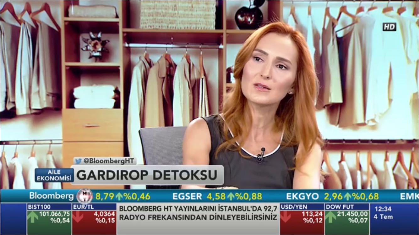Woman with red hair sitting in a clothing store, surrounded by racks of clothes, speaking on a TV show.
