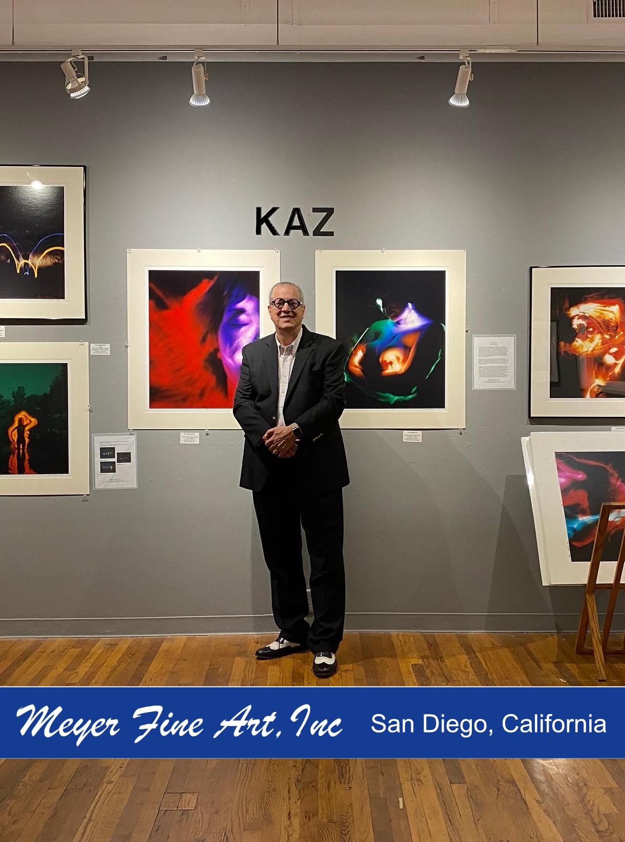 Man in suit standing in front of colorful abstract artwork at art gallery, with 'KAZ' sign above.