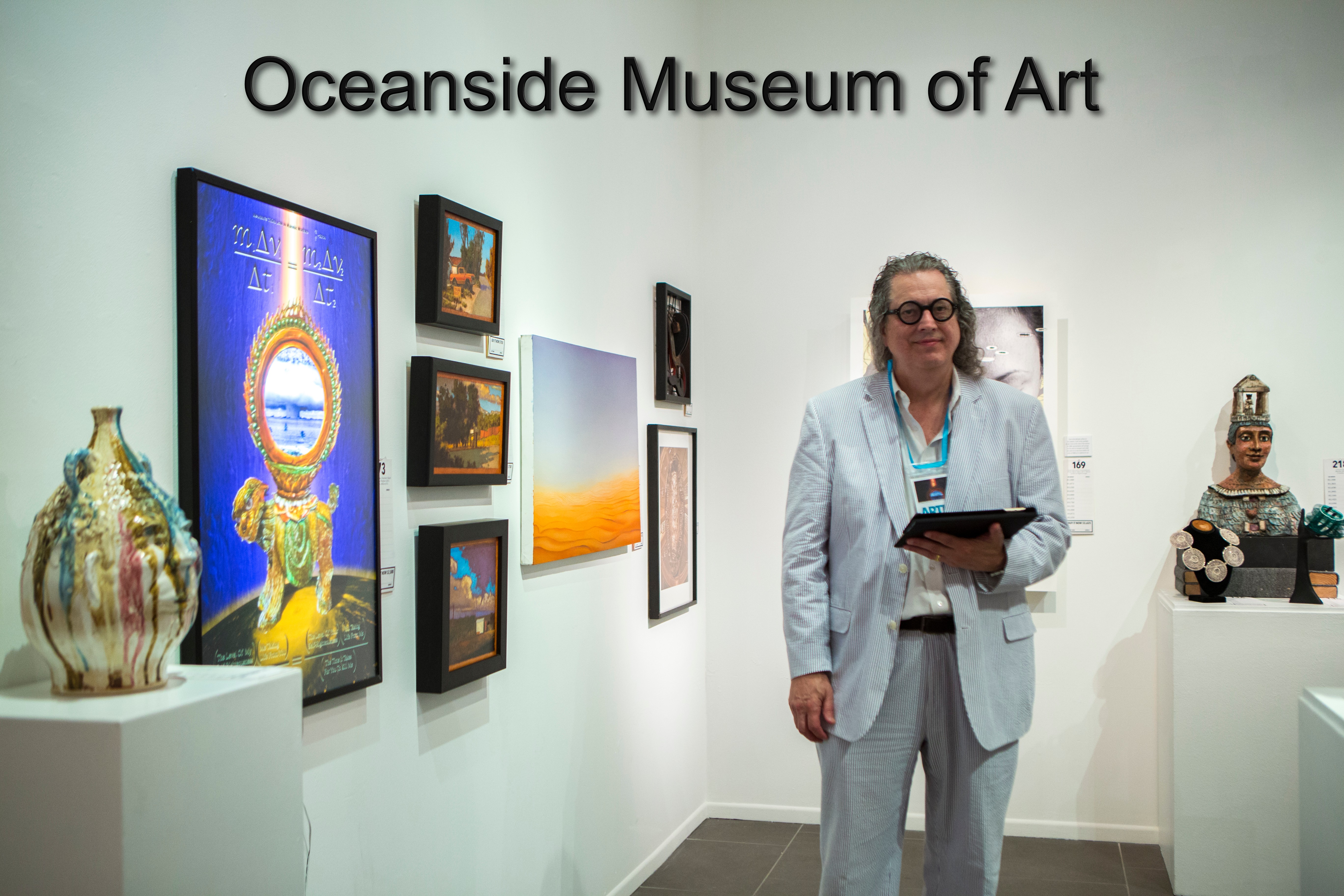Woman in light-colored suit holding a tablet in an art gallery with paintings and sculptures displayed on white walls and pedestals.