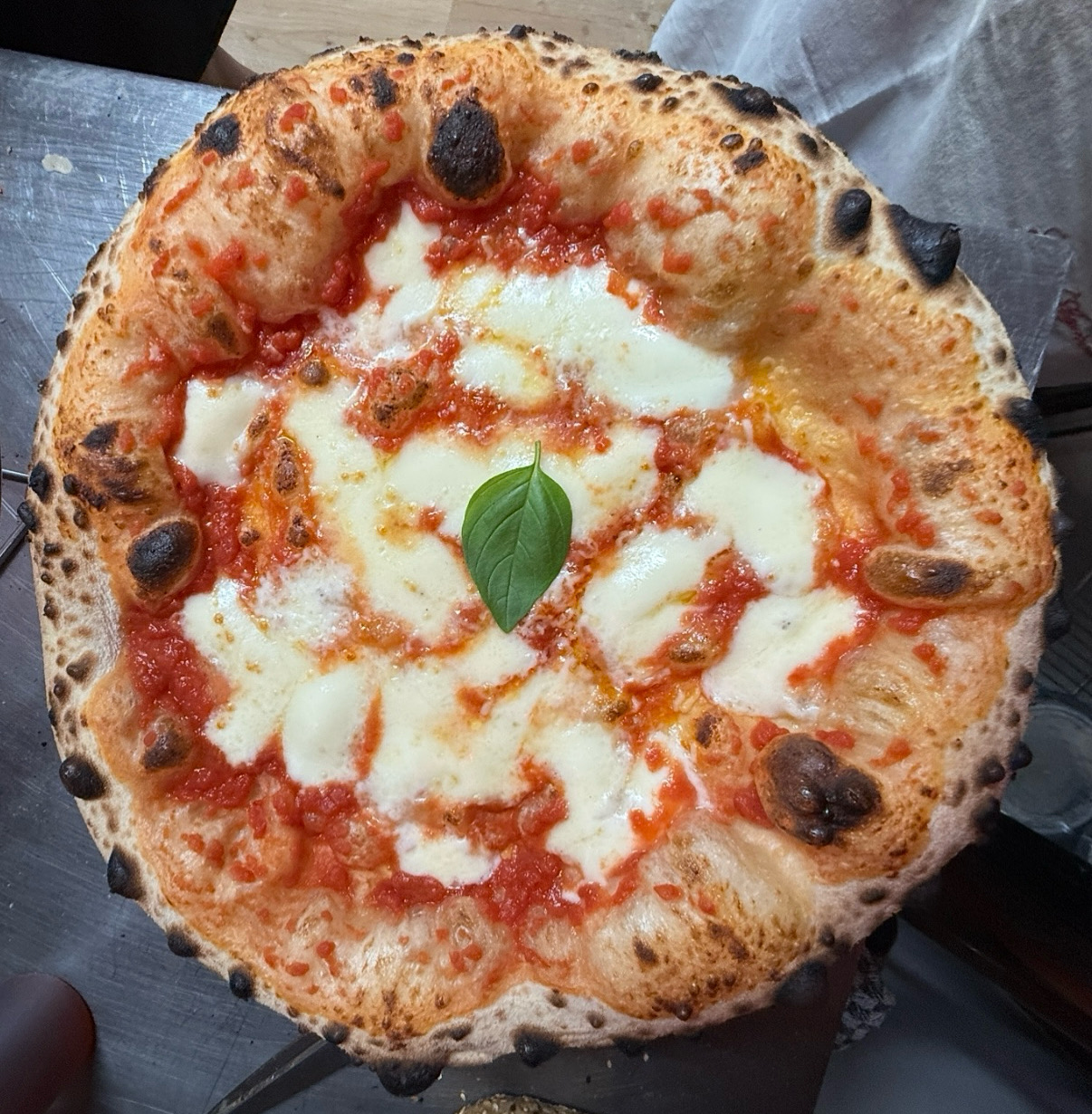 Round pizza with melted cheese, tomato sauce, and a basil leaf on top, on a gray surface.