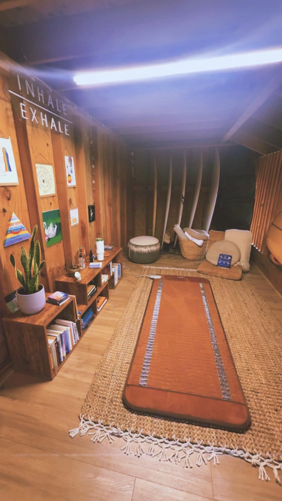 Room with wooden walls, a long orange rug, seating area, plants, and wall decorations, including a sign with text.
