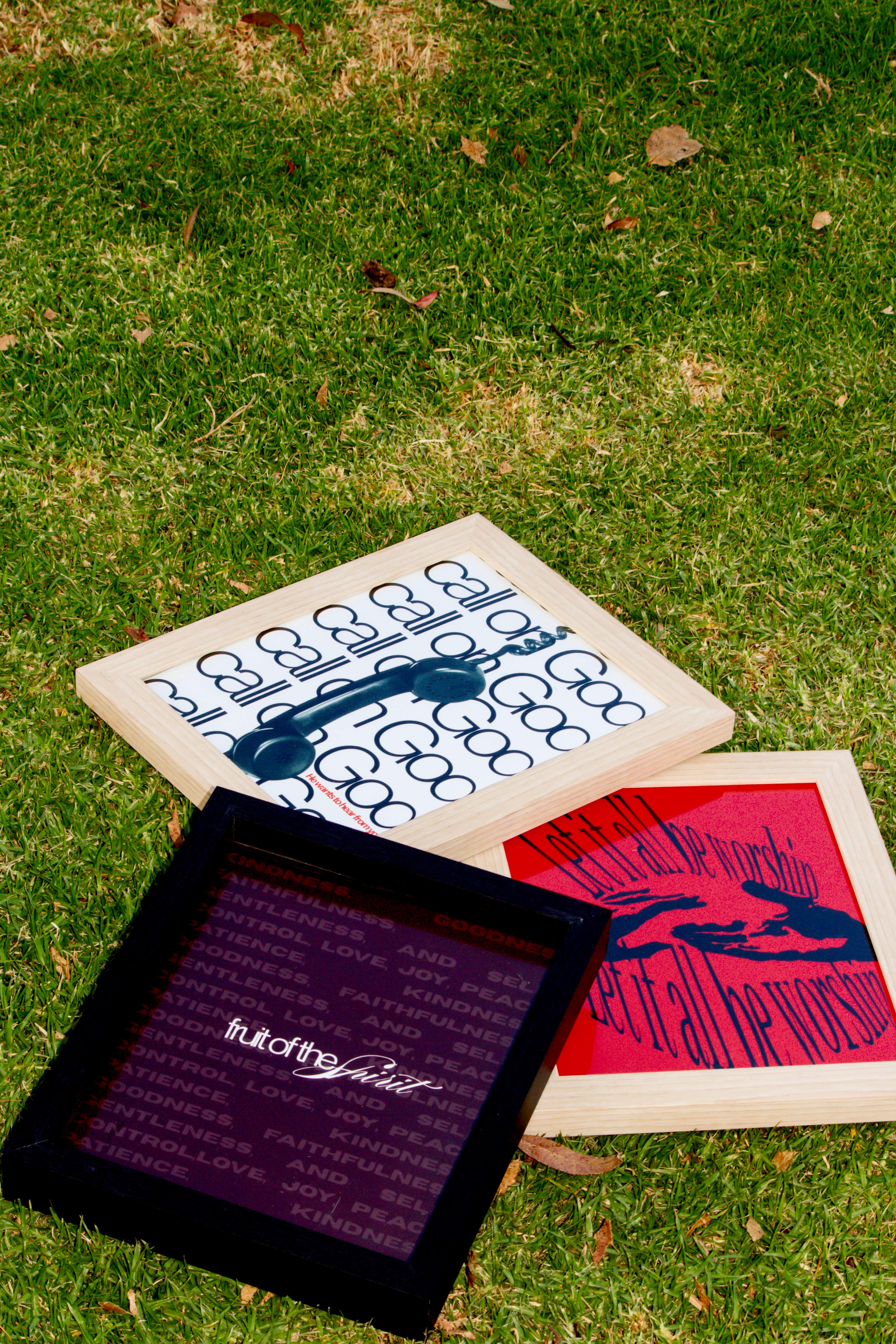Three books and a tablet on grass, with one book open showing red and black illustrations, and the tablet displaying text.