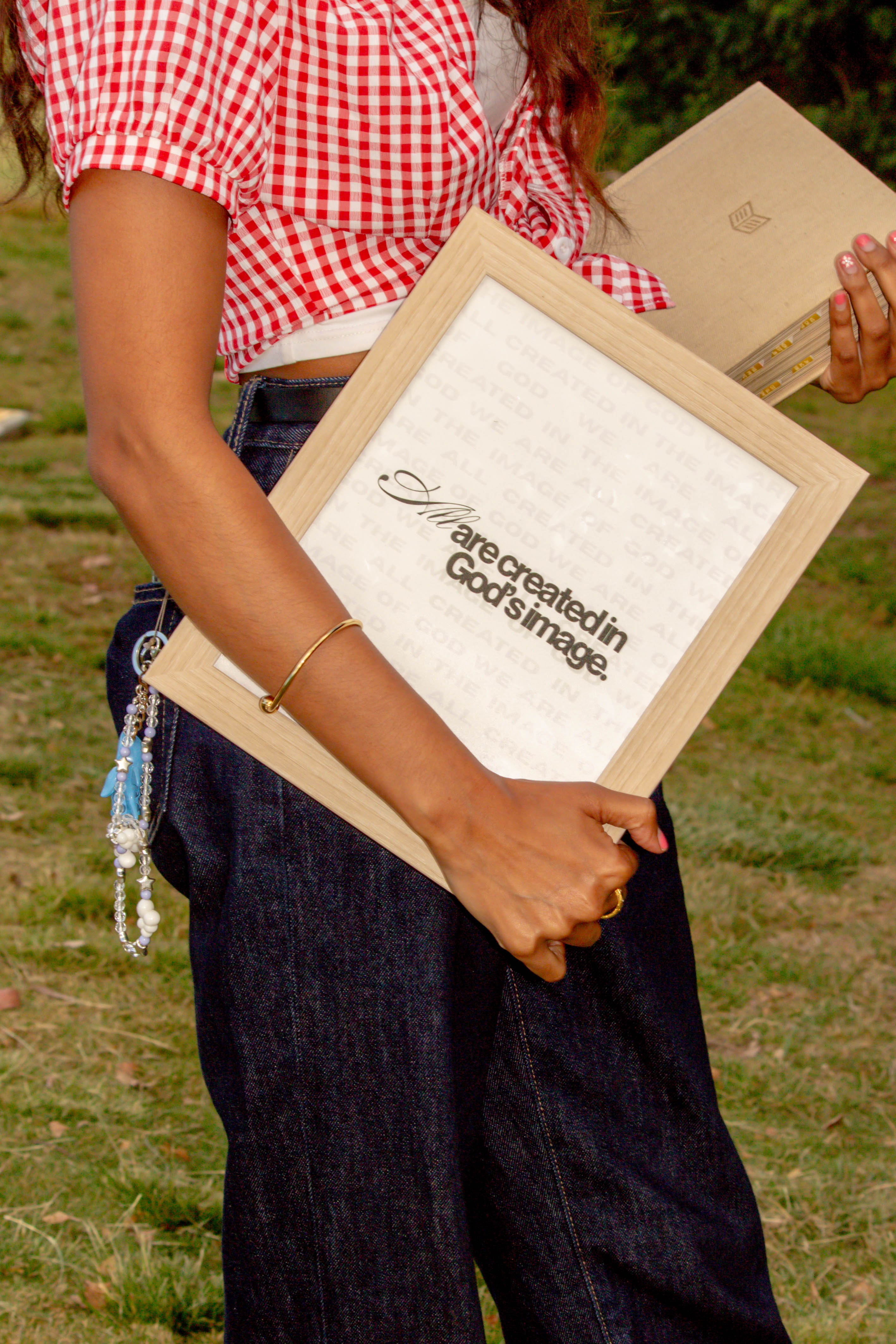 Person holding a framed certificate outdoors, wearing a red checkered shirt and dark pants.