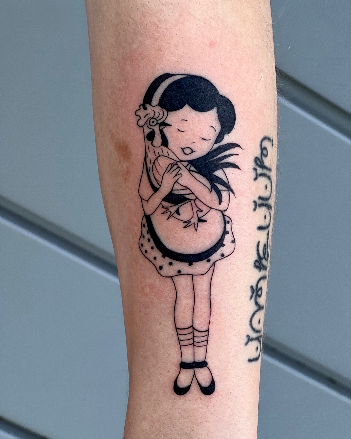 Tattoo of a girl with long hair, closed eyes, and hands together, wearing a dress and socks, with text beside.