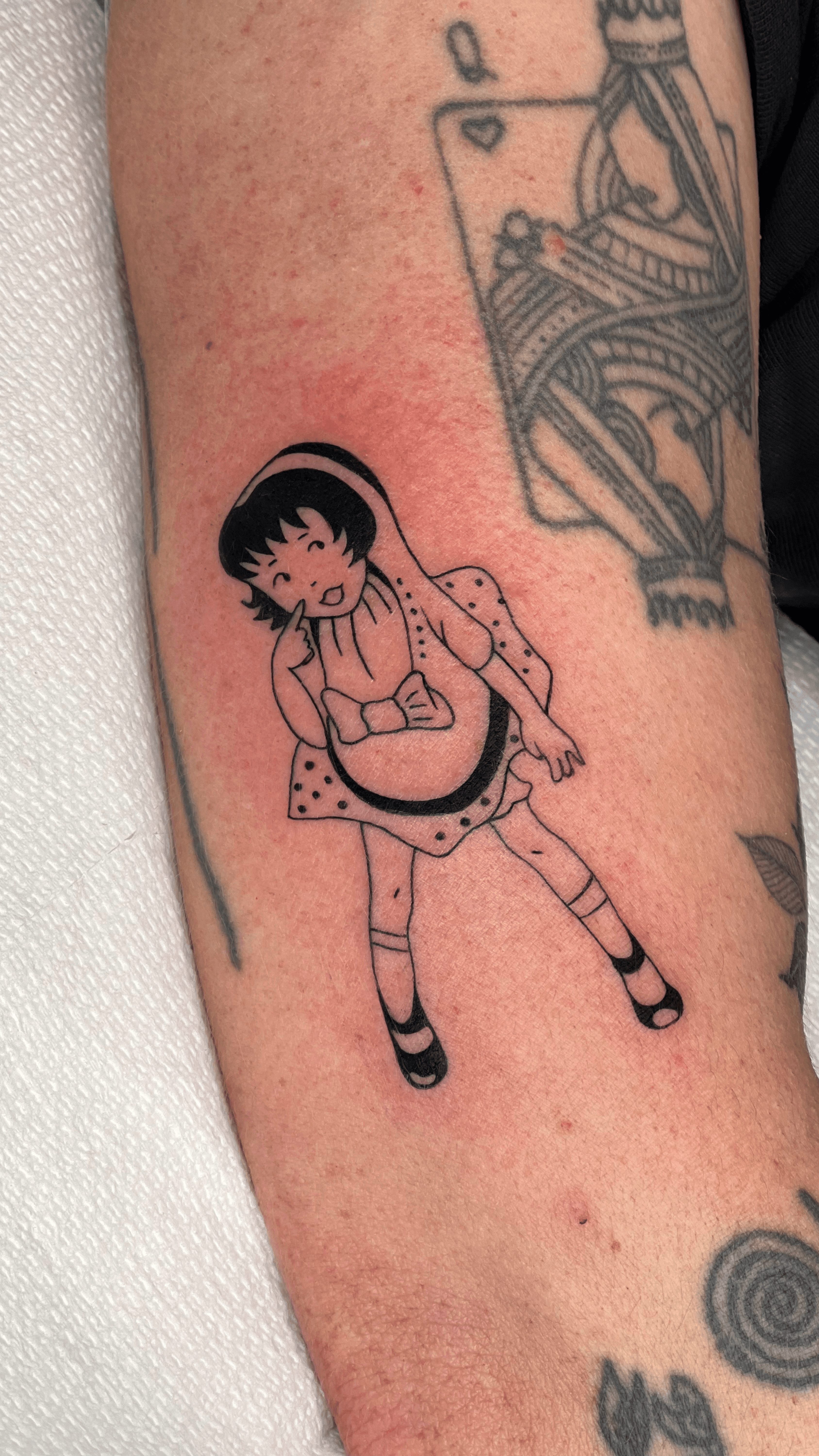 Tattoo of a girl with short hair, sitting with legs crossed, wearing a dress and striped socks.
