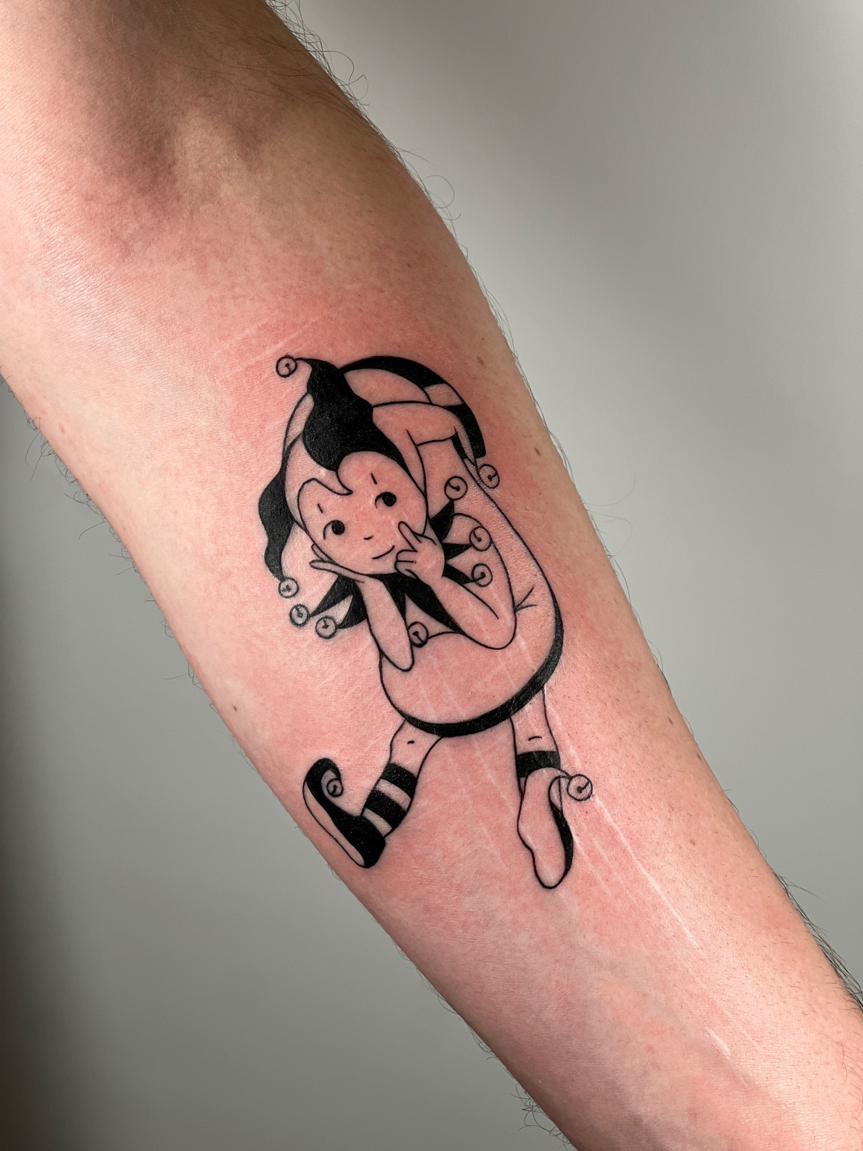 Tattoo of a cartoon girl with curly hair, wearing a dress, holding her finger to her lips, on a person's arm.