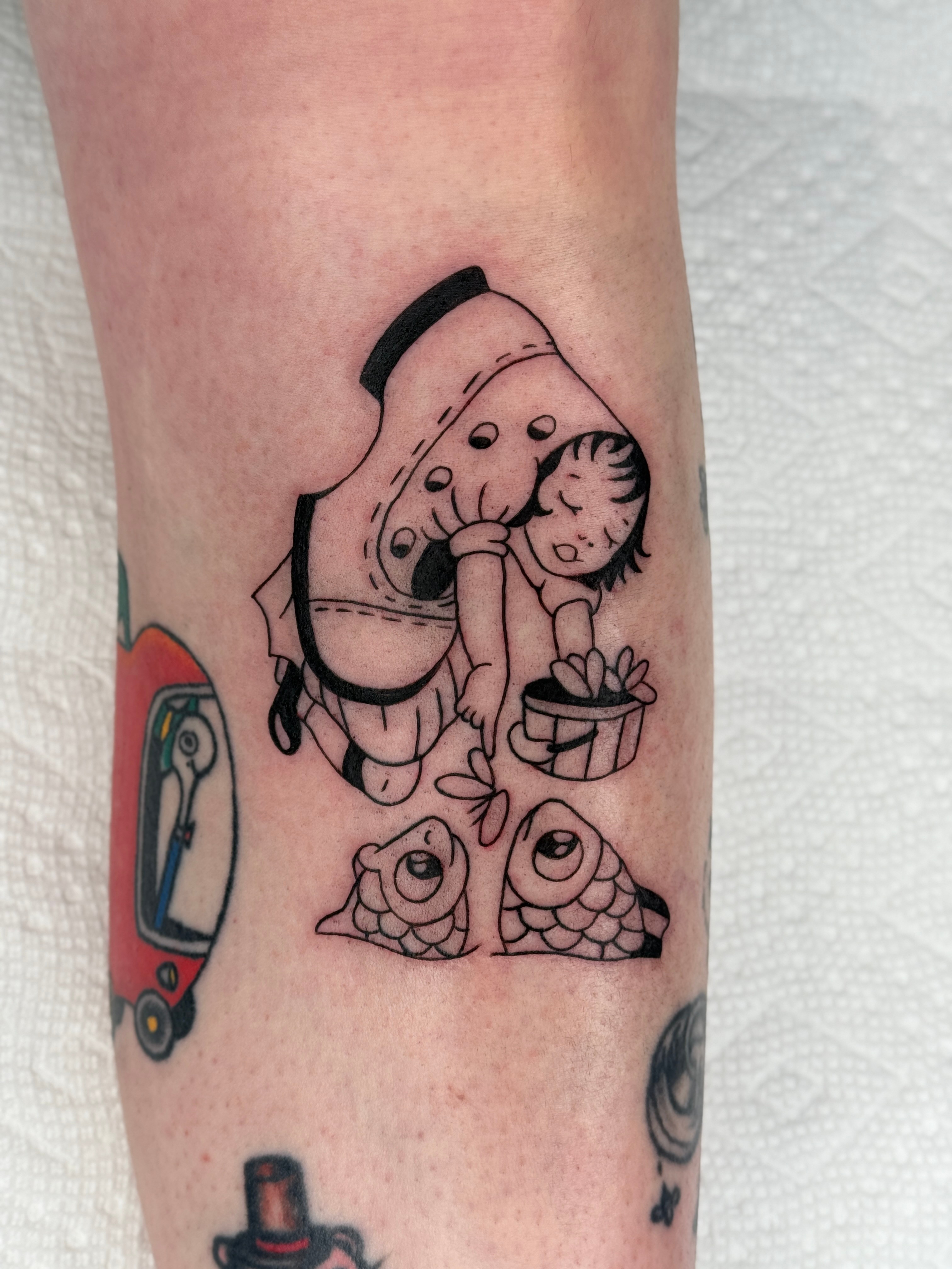 Tattoo of a girl hugging a large fish, with two smaller fish below, and a gift box nearby.
