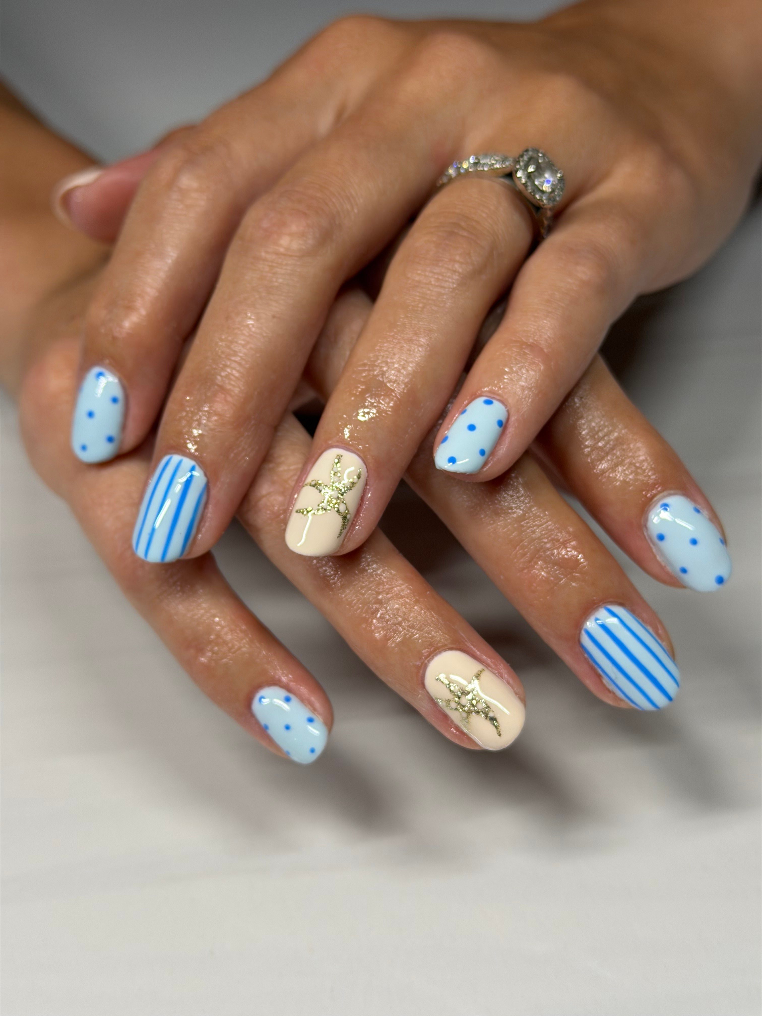 Close-up of hands with decorated nails, featuring blue and white striped and polka dot patterns, and a ring on the finger.