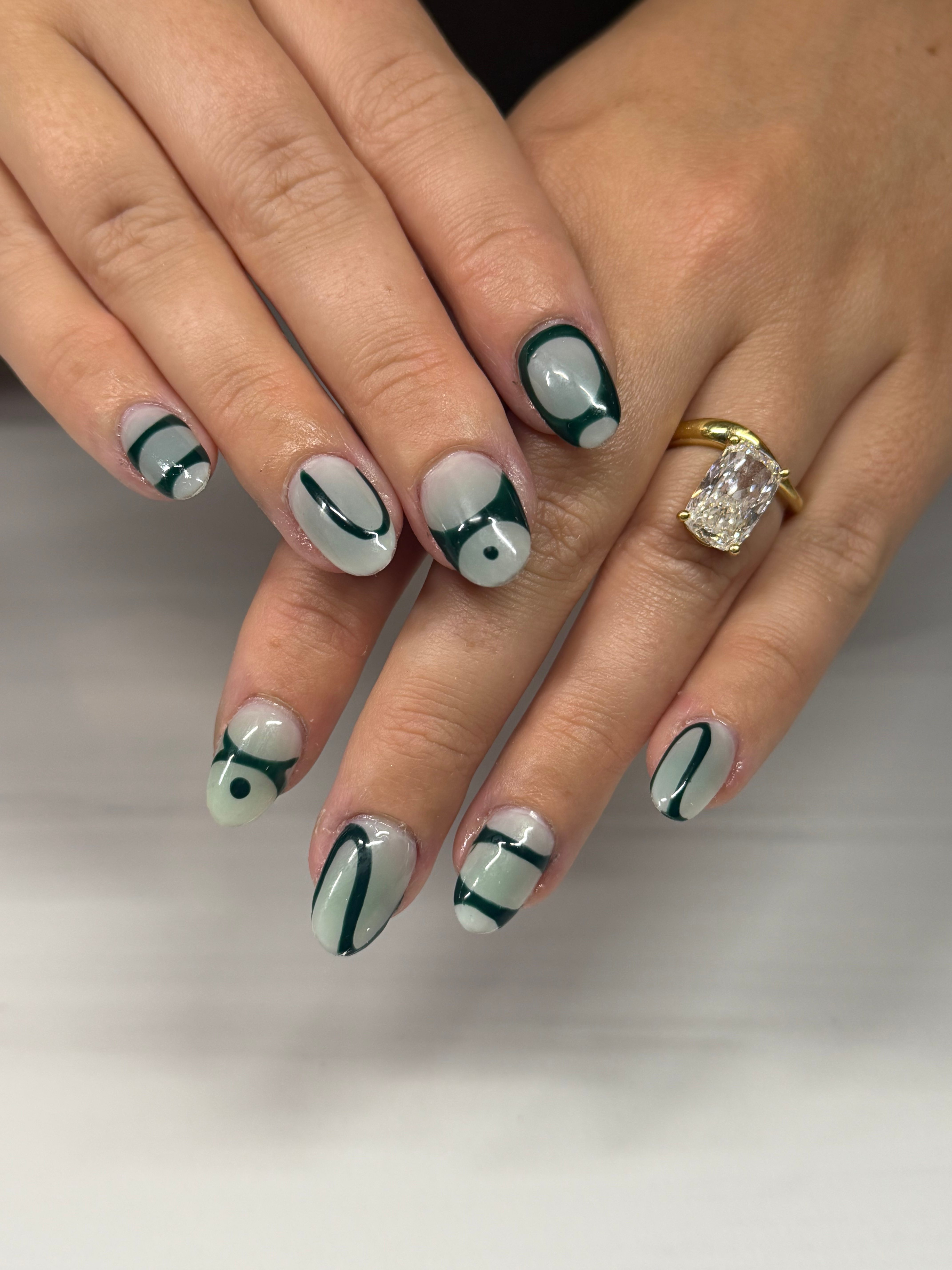 Hands with decorated nails and a ring, nails have abstract black, white, and gray designs.
