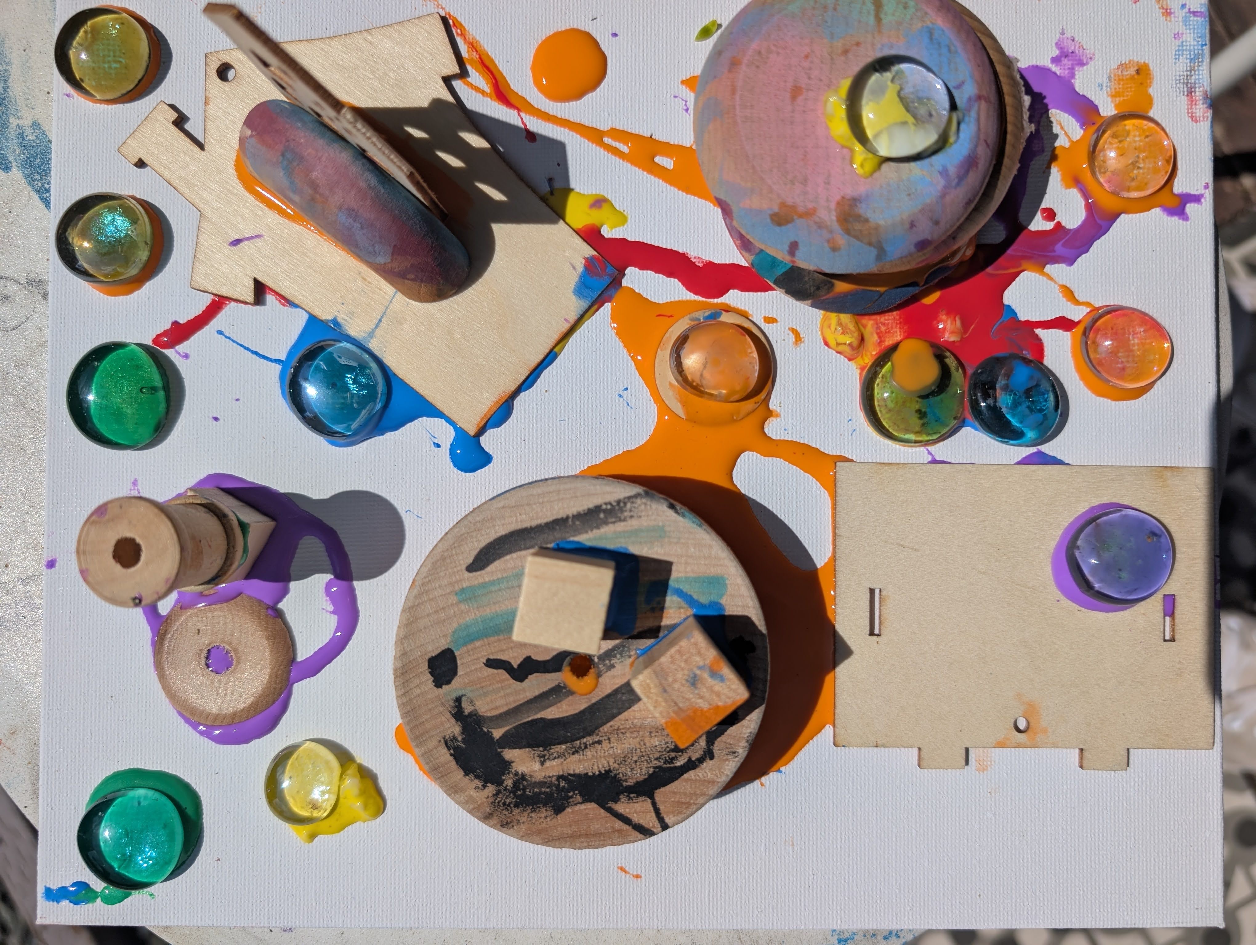 Colorful paint splatters and circular objects on a white surface with wooden pieces and small containers of paint.