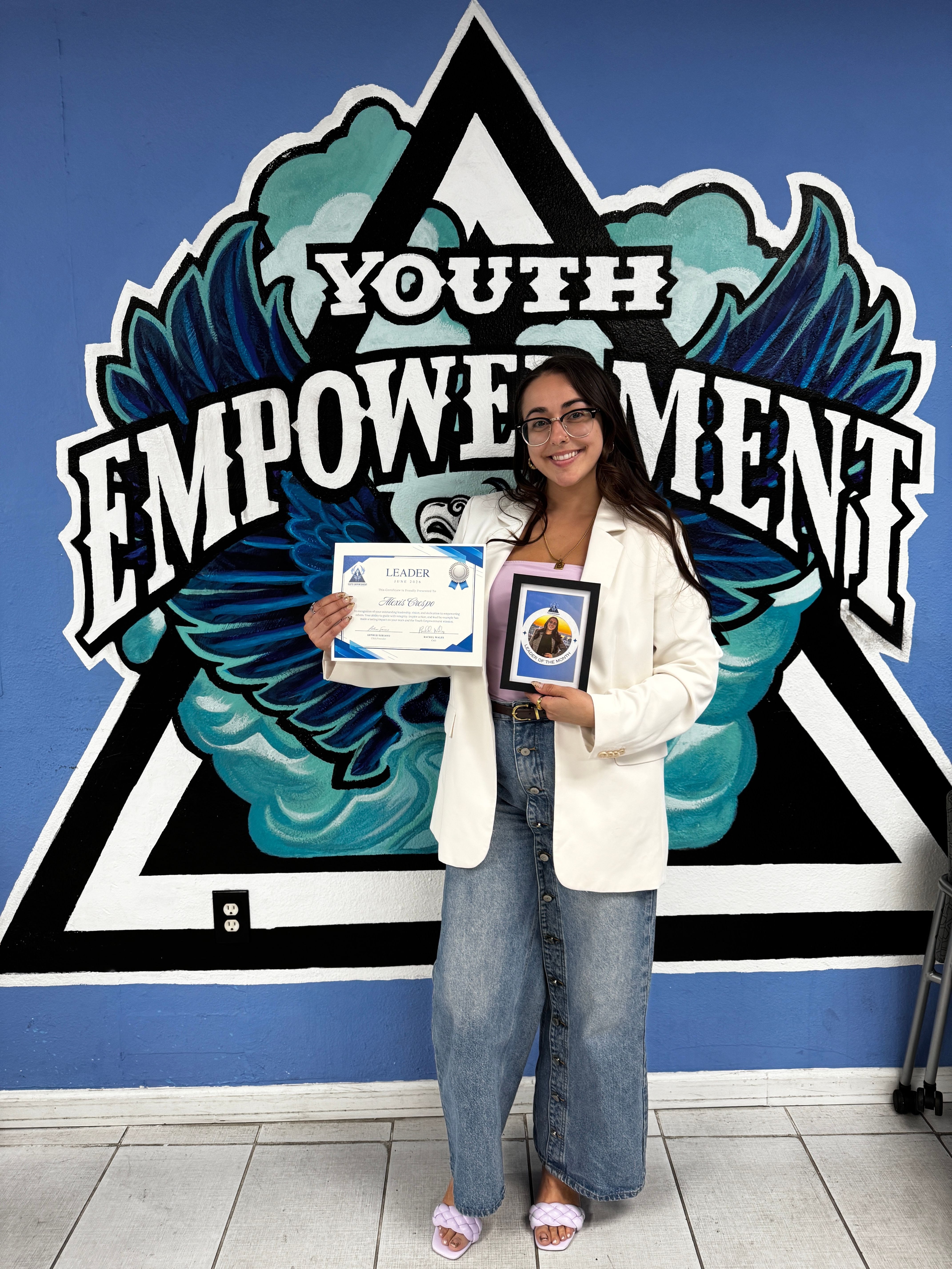 Person holding a certificate and a plaque standing in front of a mural with text and graphics.