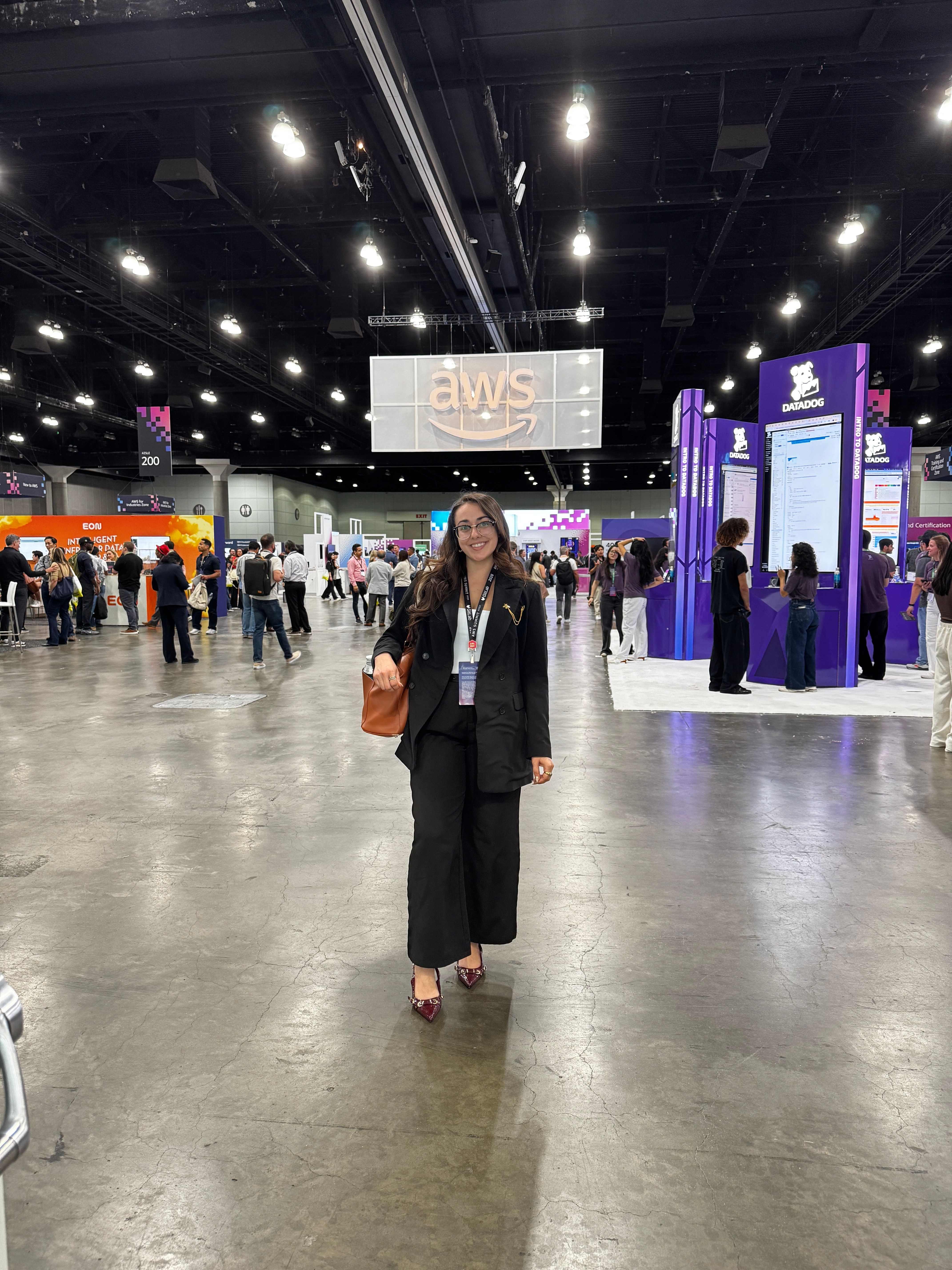 Two women standing in a conference hall with digital screens and booths in the background.