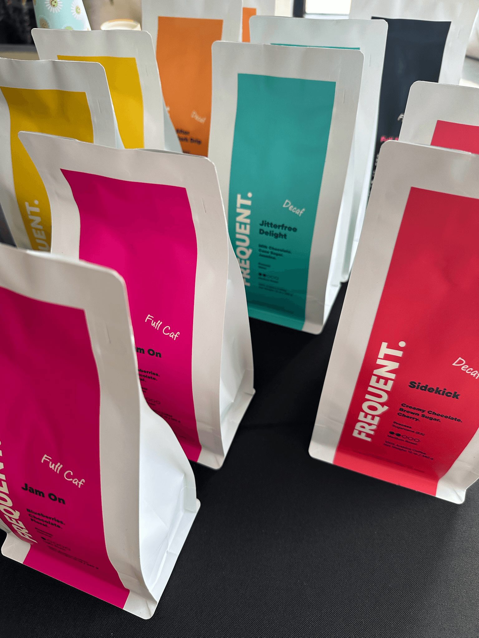 Multiple colorful packages standing upright on a black surface, with various colors including pink, teal, orange, and white.