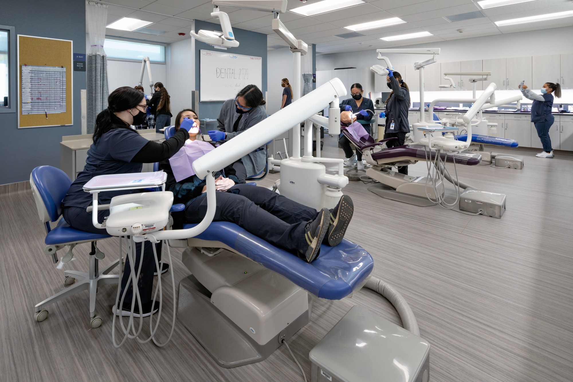 Dental students practicing procedures on patients in a modern clinic with dental chairs and equipment.