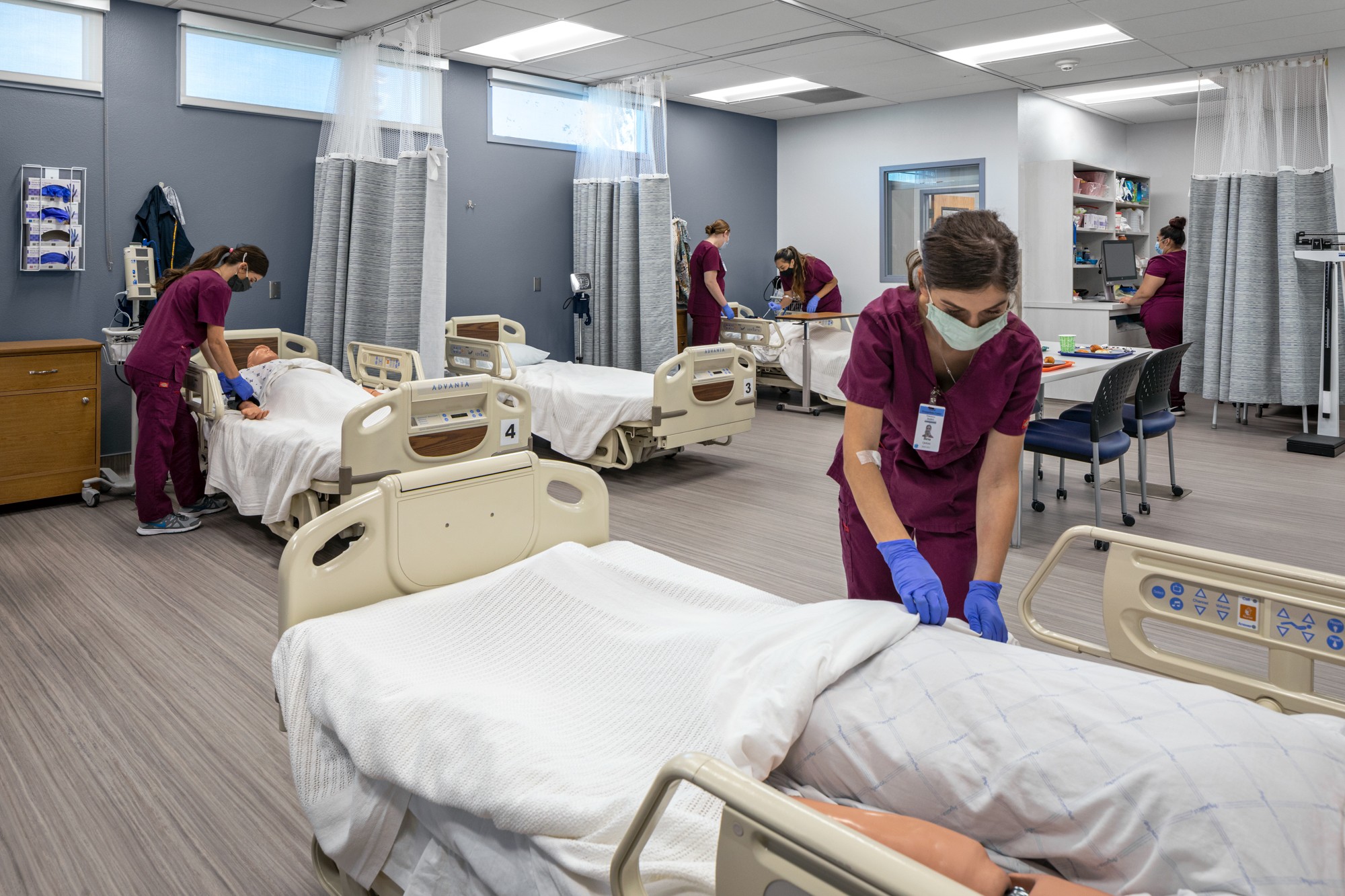 Hospital room with nurses preparing beds and attending to patients, medical equipment, and privacy curtains, bright and clean environment.