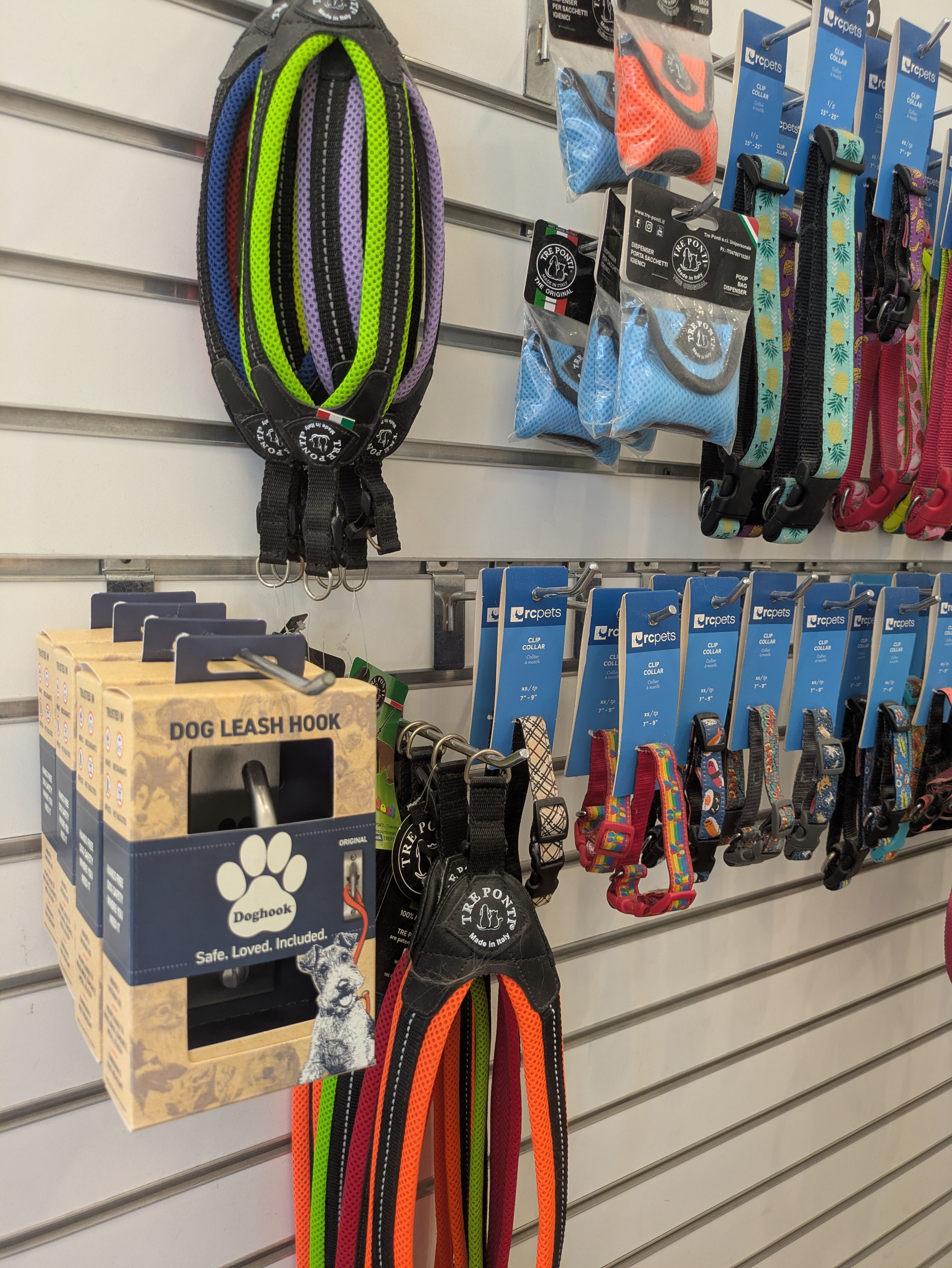 Dog leash hooks and collars displayed on a store wall, with a colorful dog harness hanging above.