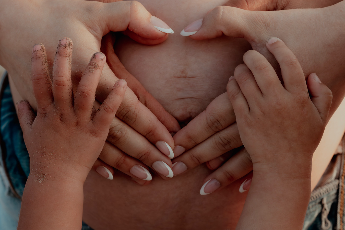 Multiple hands form a heart shape on a person's abdomen, with visible skin and nails.