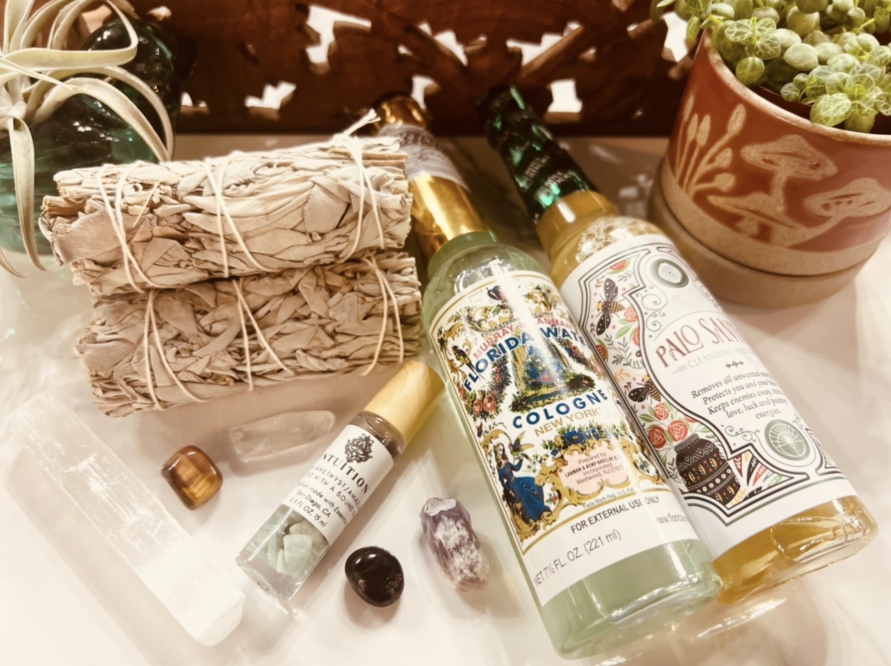 Assorted bottles, a bundle of sage, and a potted plant on a white surface.